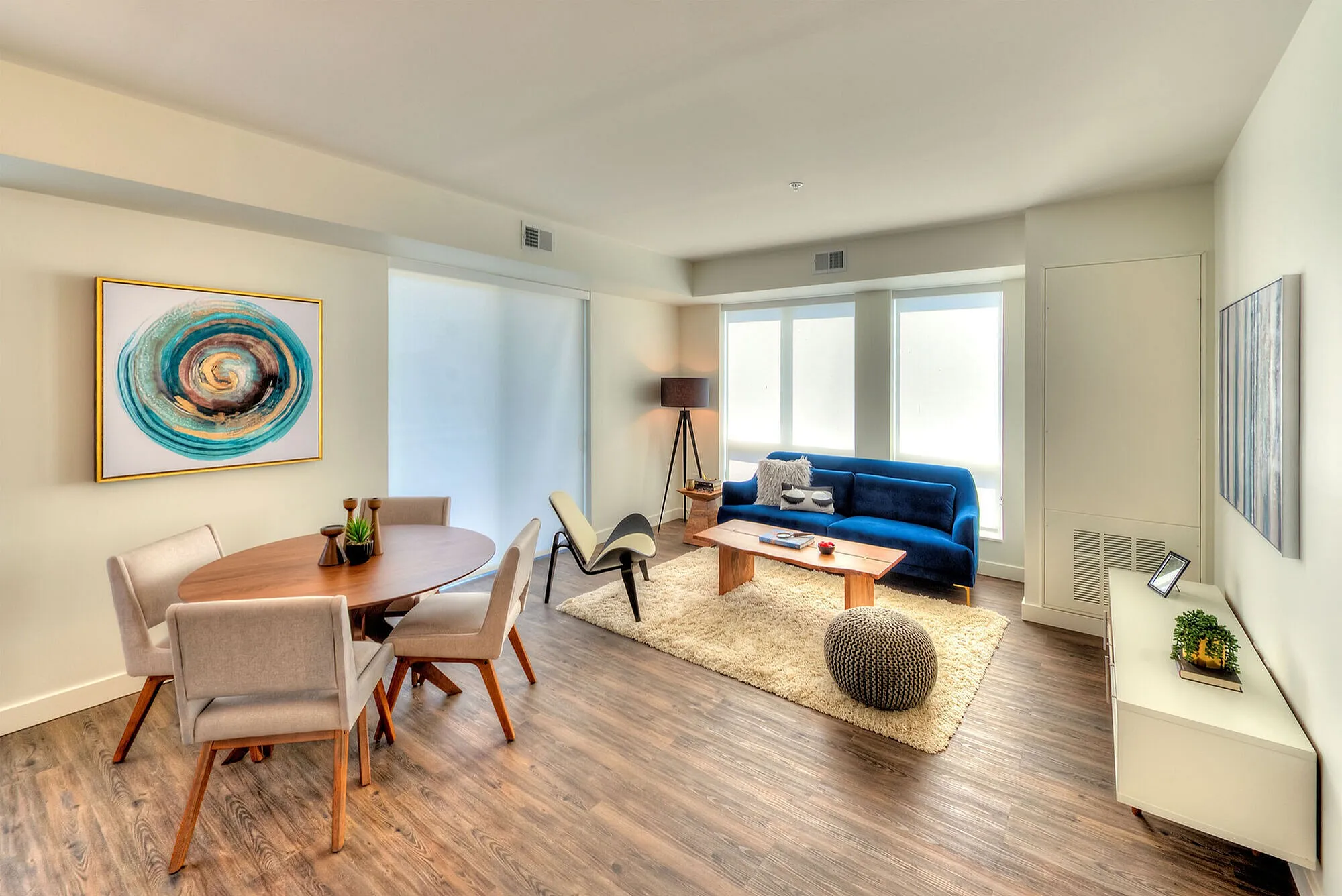 Modern living room with elegant decor featuring a sleek blue sofa, stylish dining area, and warm wooden flooring.