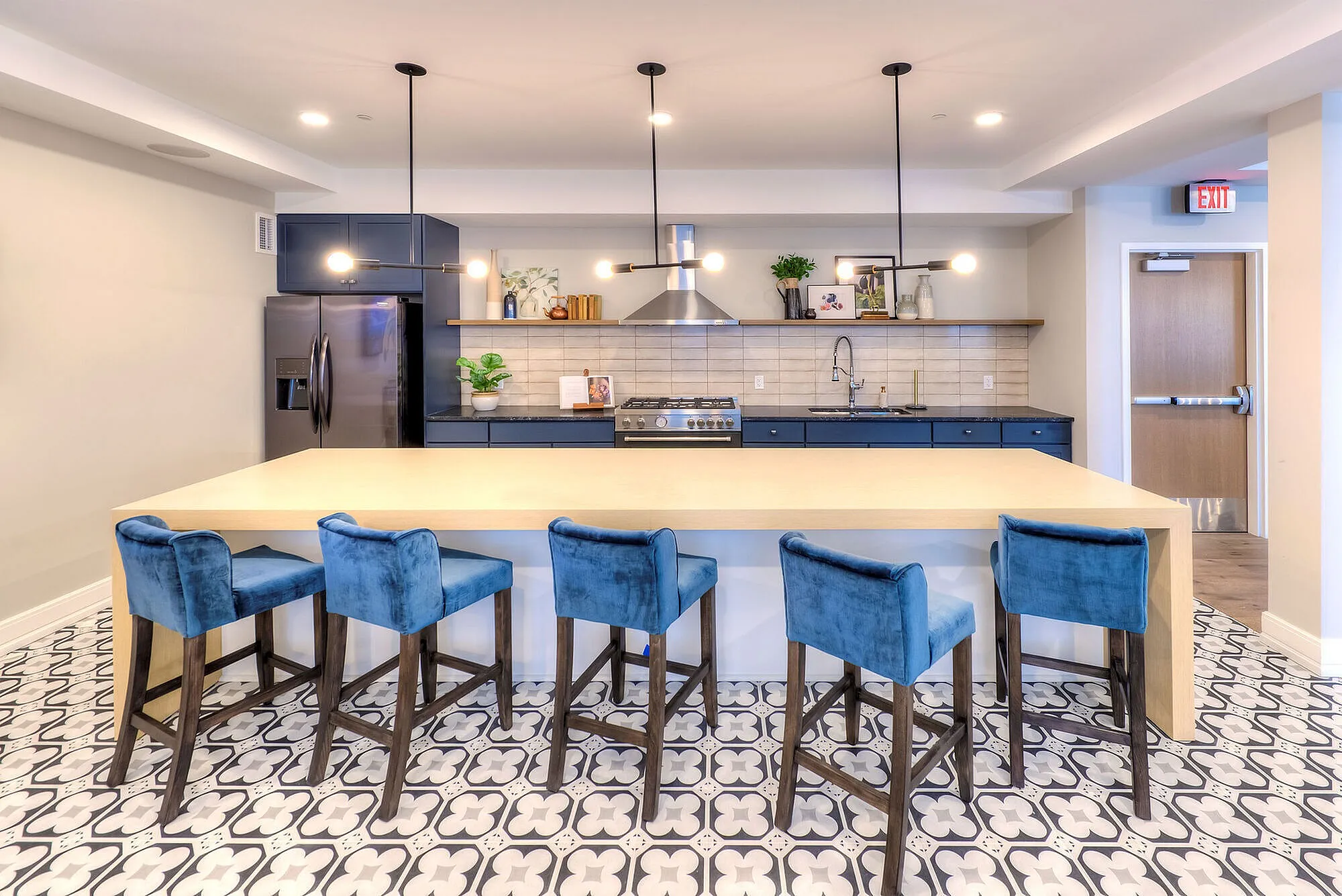 Chic modern kitchen with vibrant blue velvet chairs, spacious island, stylish pendant lights, and sleek stainless steel appliances on patterned tile flooring.