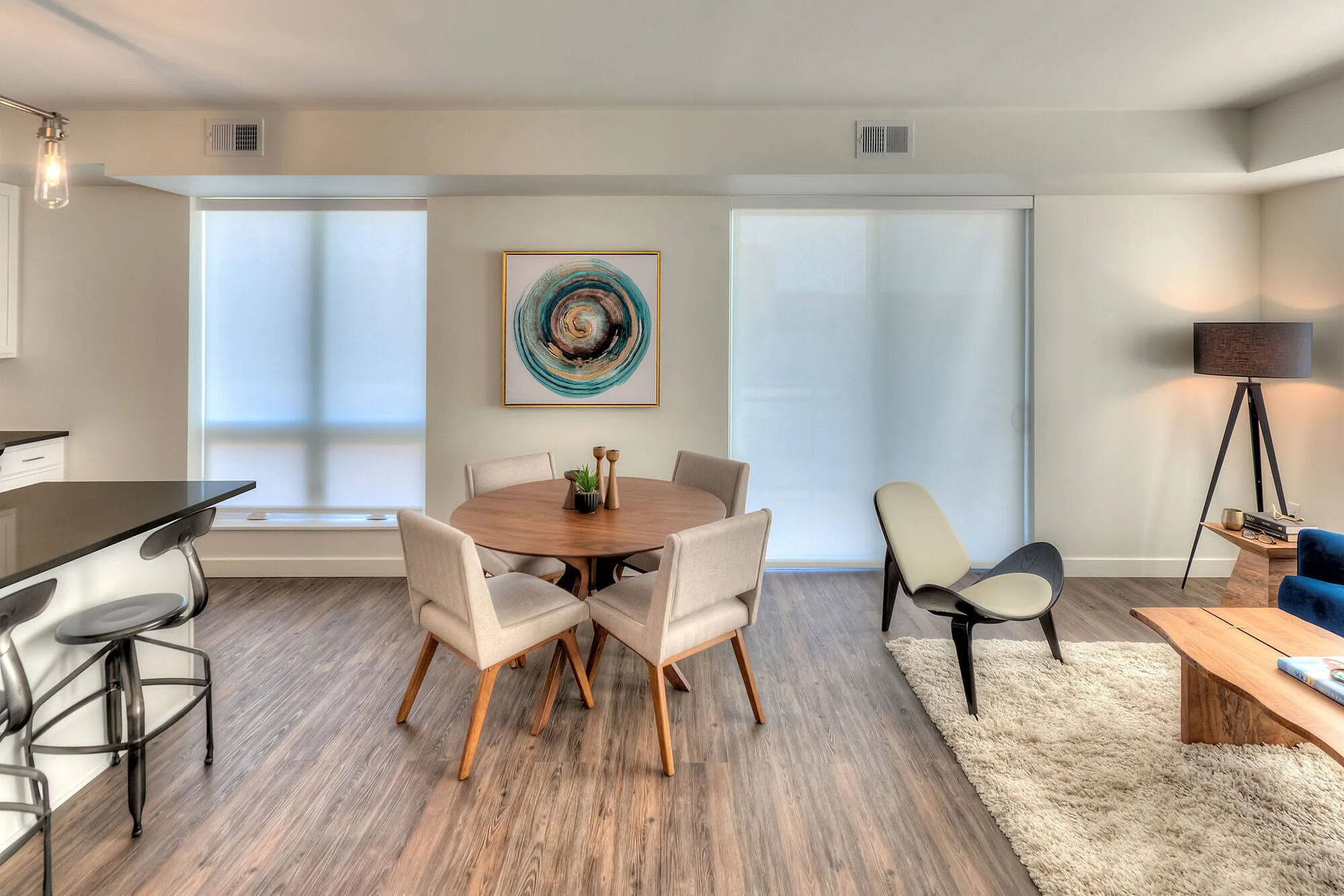 Modern open-plan living area with stylish furnishings, featuring a round wooden dining table, cozy plush rug, and elegant decor accents.