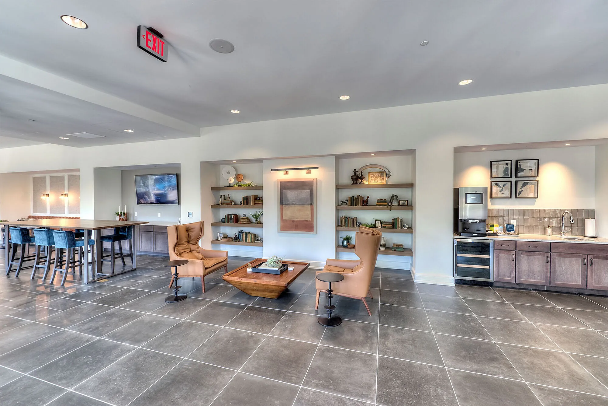 Modern communal living space with sleek tile flooring, stylish seating, open shelving, and a well-equipped kitchenette.