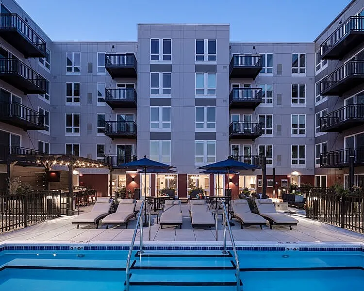 Modern apartment complex with a luxurious pool area at twilight, featuring comfortable lounge chairs and elegant balconies.