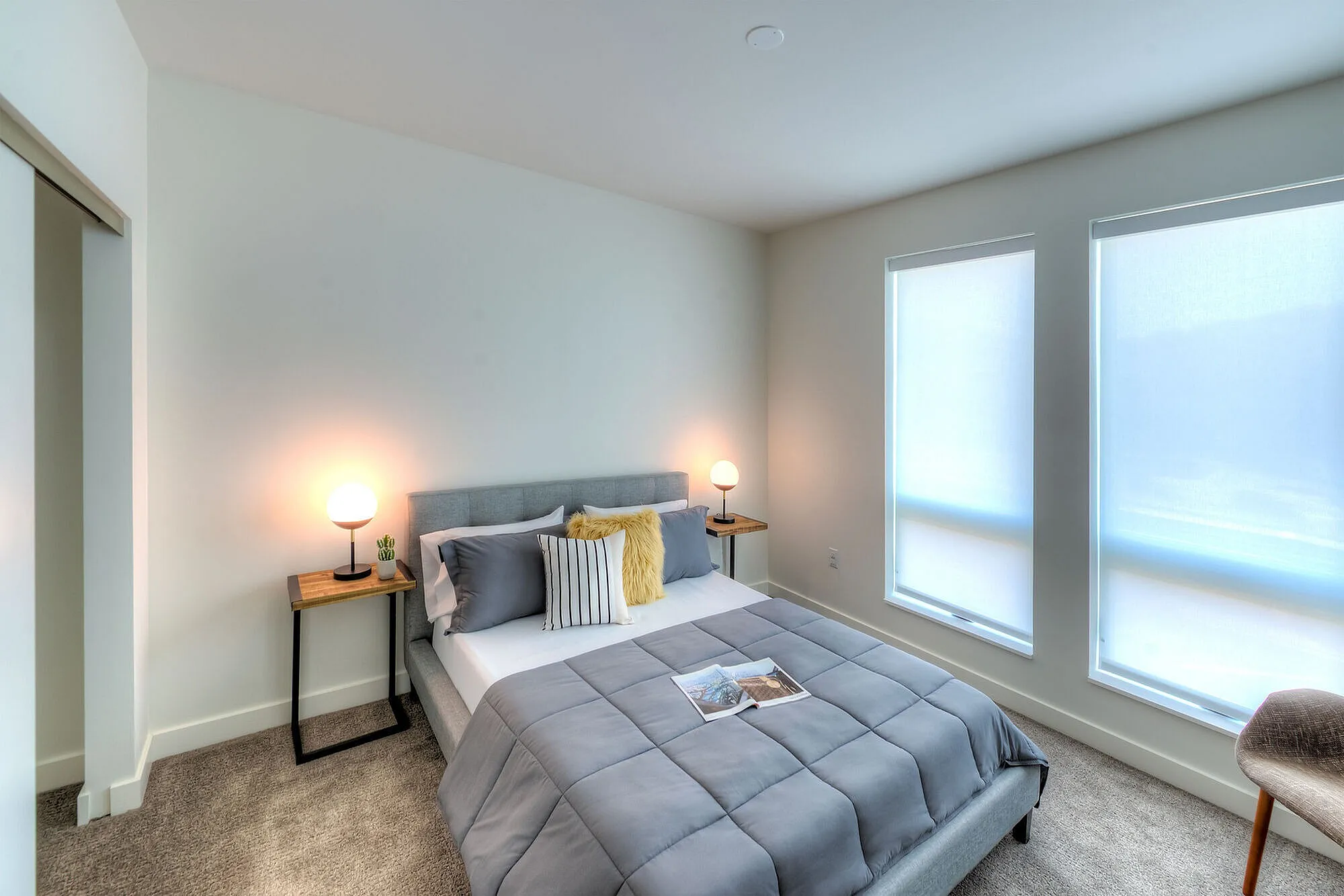 Inviting bedroom with modern décor, featuring a plush gray bedspread, stylish accent pillows, and warm lighting from sleek bedside tables.