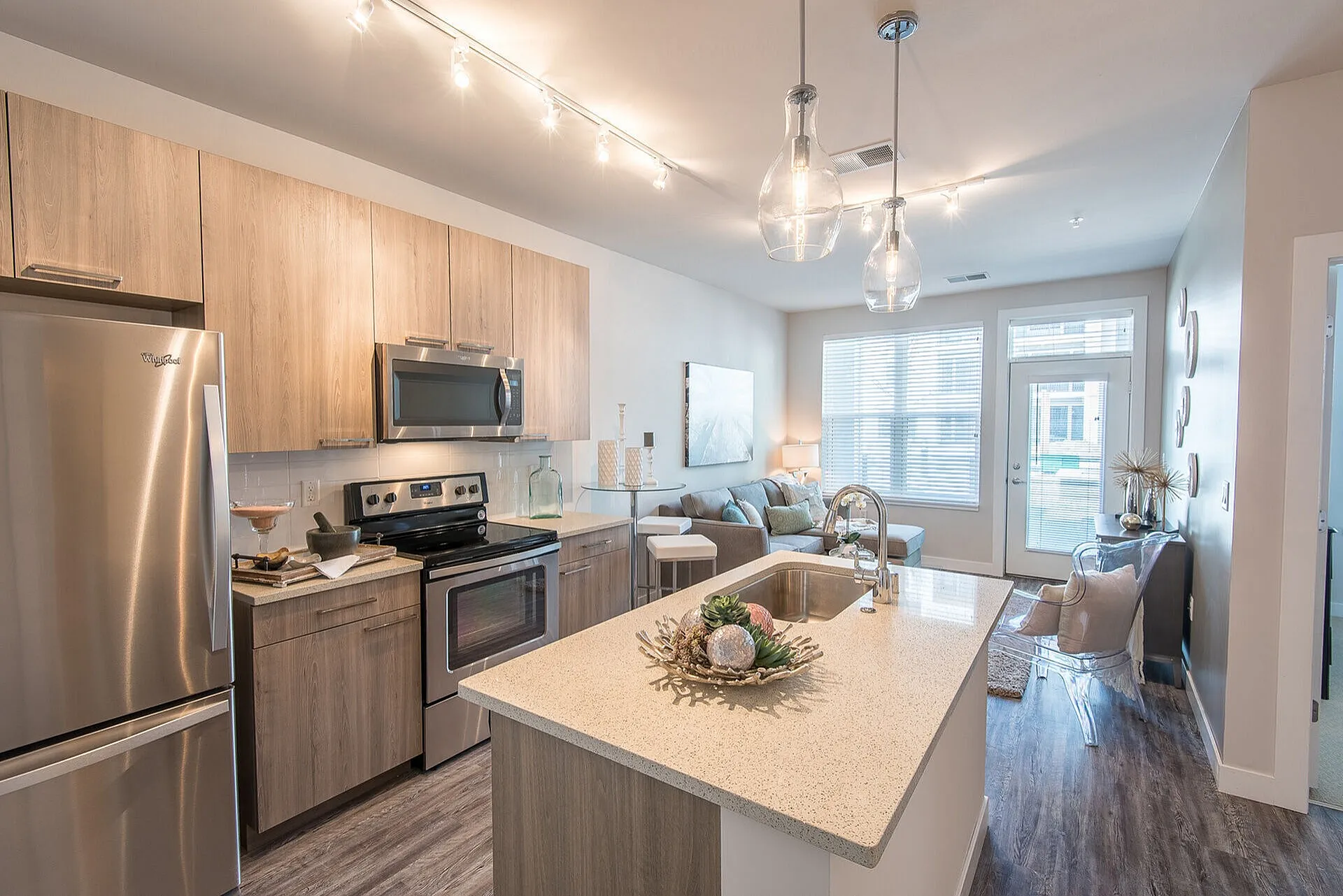 Modern open-plan kitchen and living area with stainless steel appliances, quartz countertops, and elegant lighting fixtures.