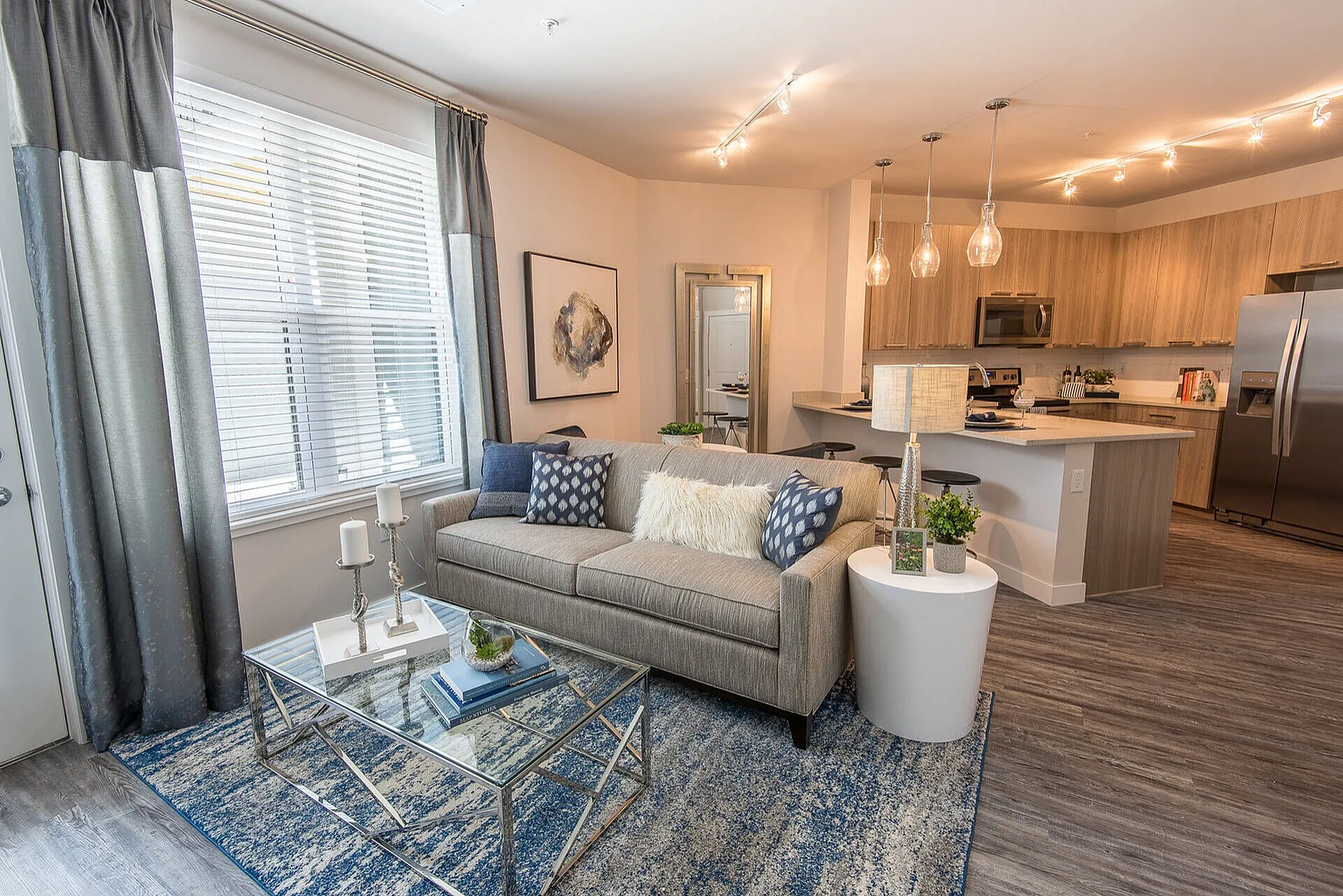 Modern open-concept living space featuring a cozy sofa, stylish glass coffee table, elegant wooden kitchen cabinets, and chic pendant lighting.