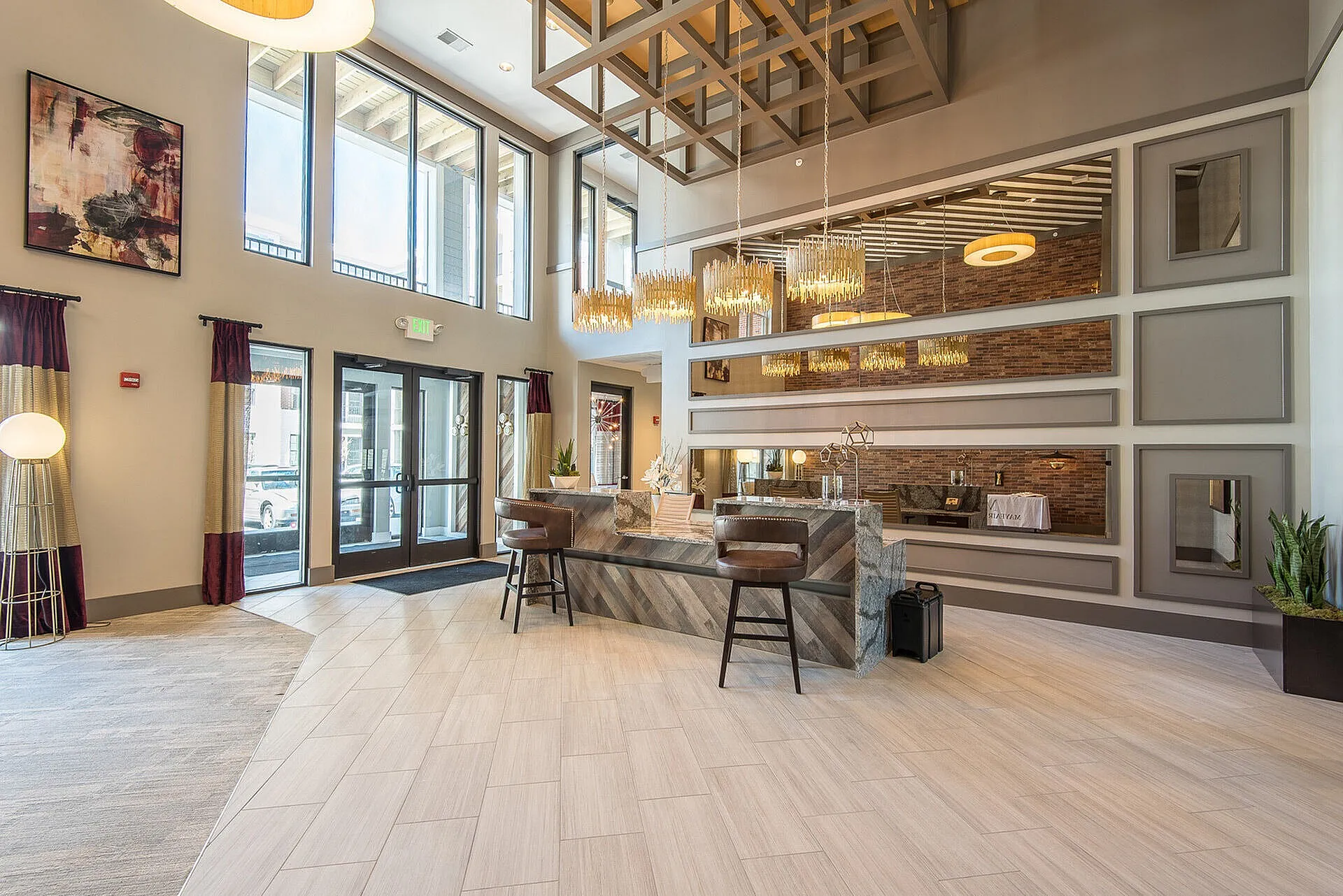 Luxurious apartment lobby with high ceilings, modern chandeliers, sleek seating area, and large windows offering abundant natural light.
