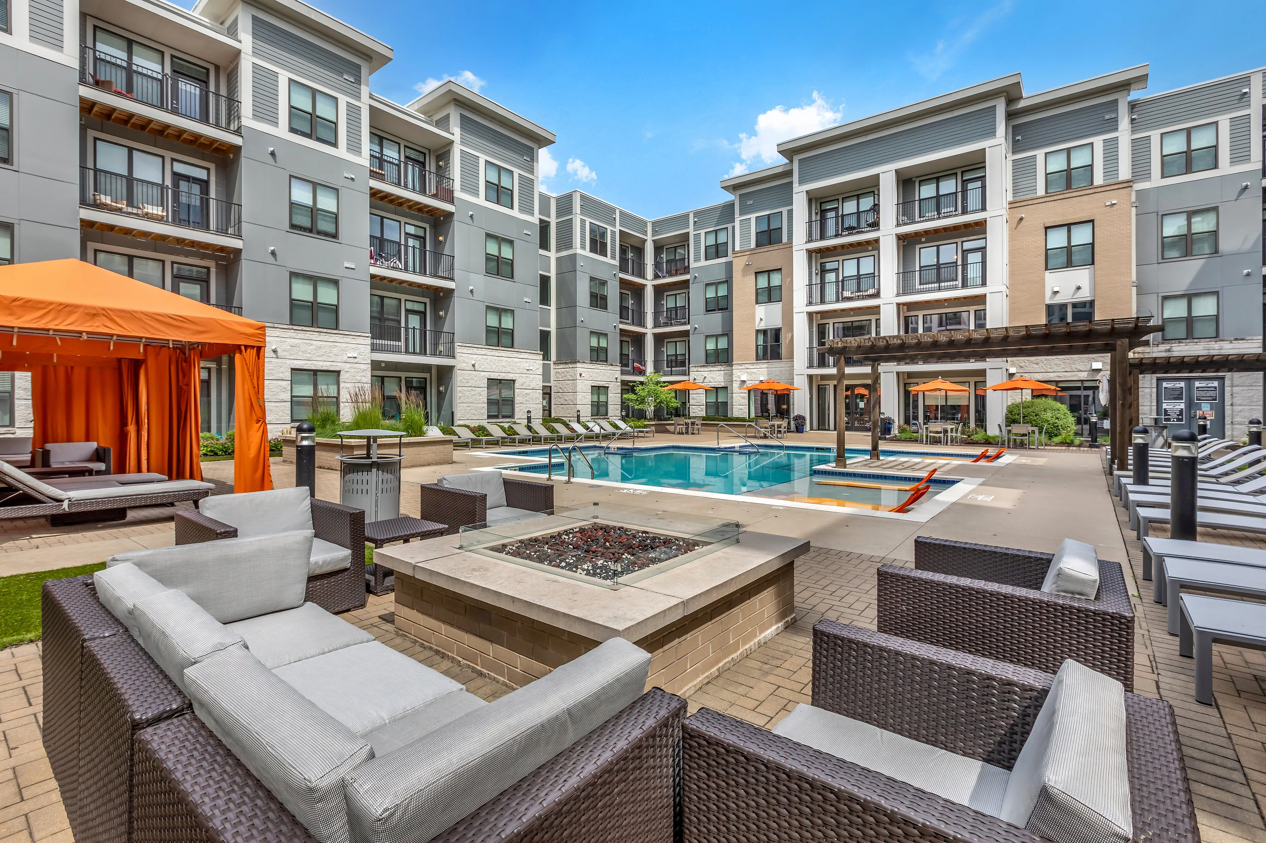 Modern apartment courtyard featuring luxurious poolside seating, vibrant orange cabanas, and a sparkling pool surrounded by stylish multi-story buildings.