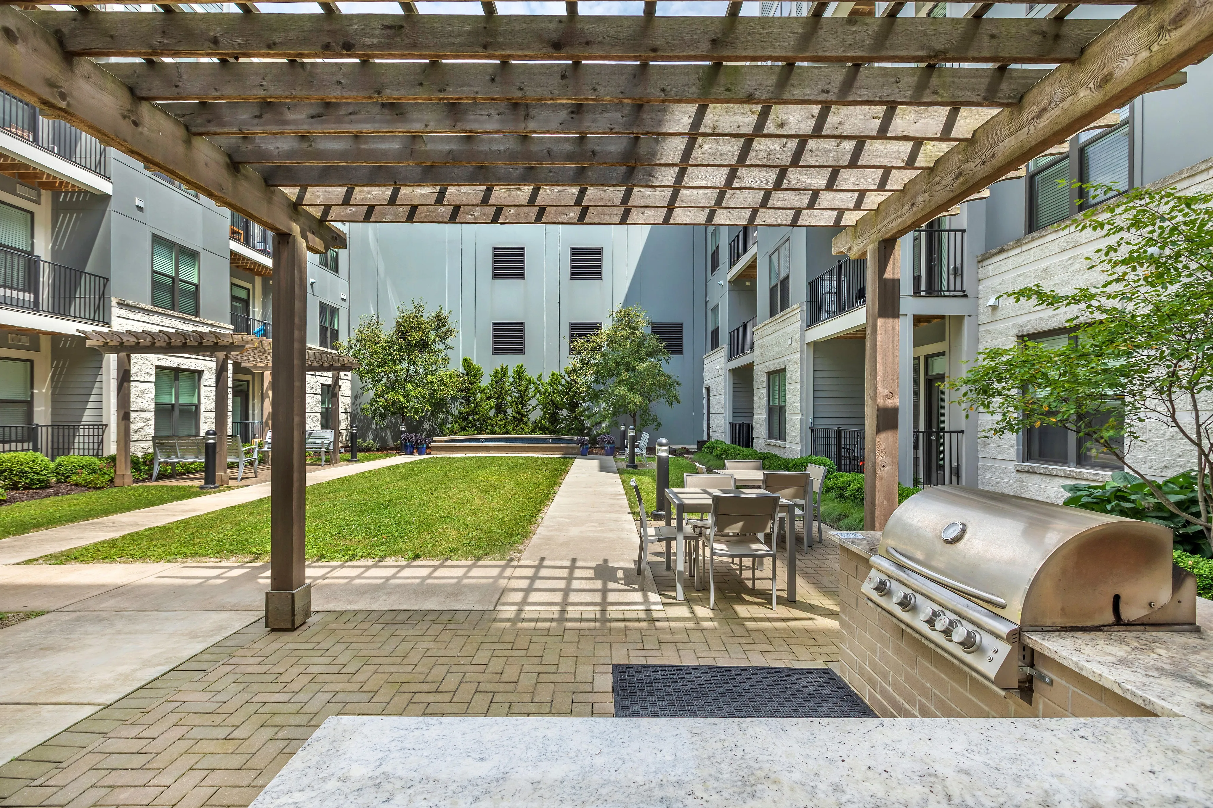 Charming apartment courtyard with outdoor dining area, BBQ grill, and lush greenery under a cozy pergola.