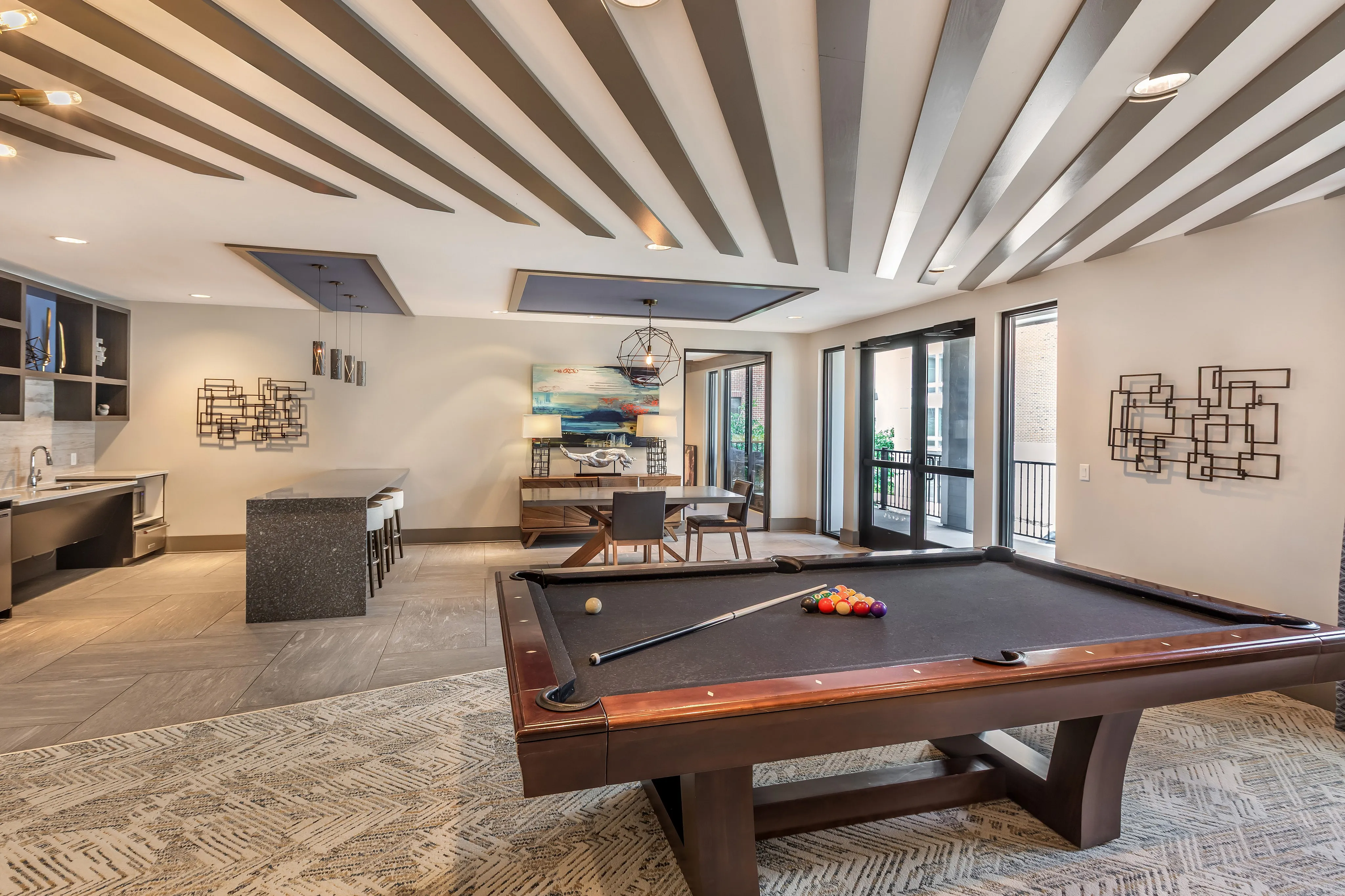 Elegant recreational room with a modern pool table, sleek bar area, and stylish decor with natural light streaming through large windows.