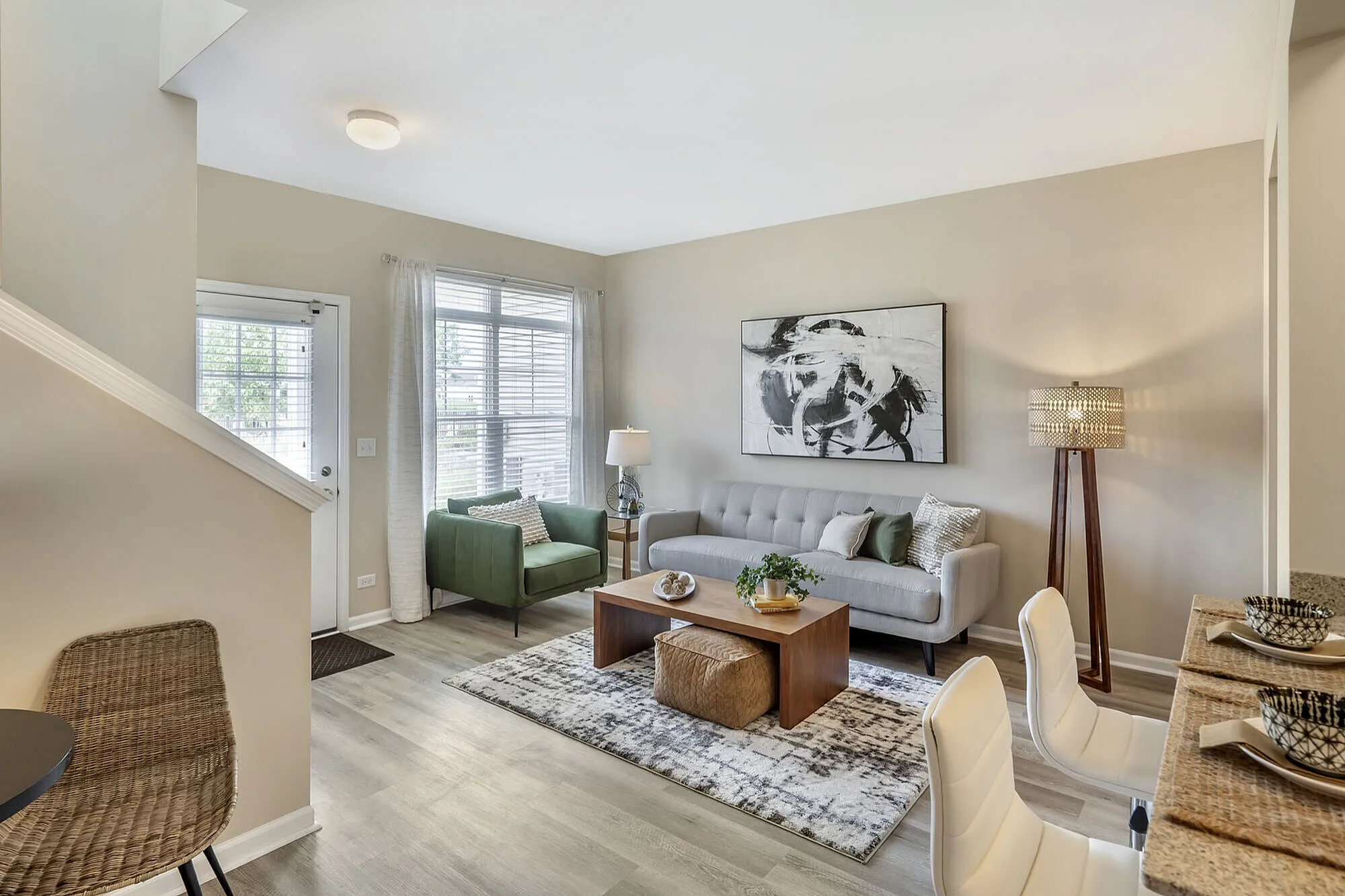 Elegant living room with modern decor, featuring a cozy gray sofa, green armchair, chic artwork, and natural light pouring through large windows.