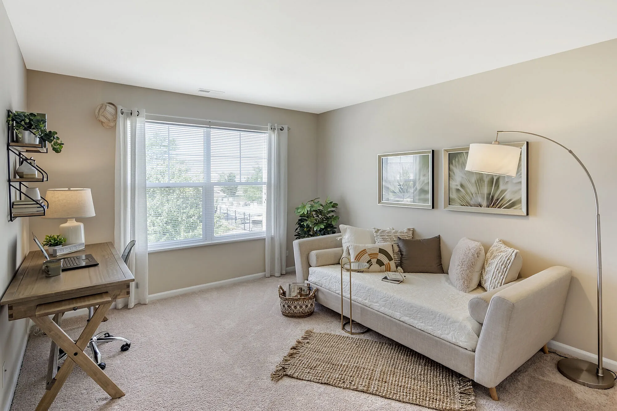 Bright and welcoming home office with large window, stylish beige sofa, and elegant wooden desk.