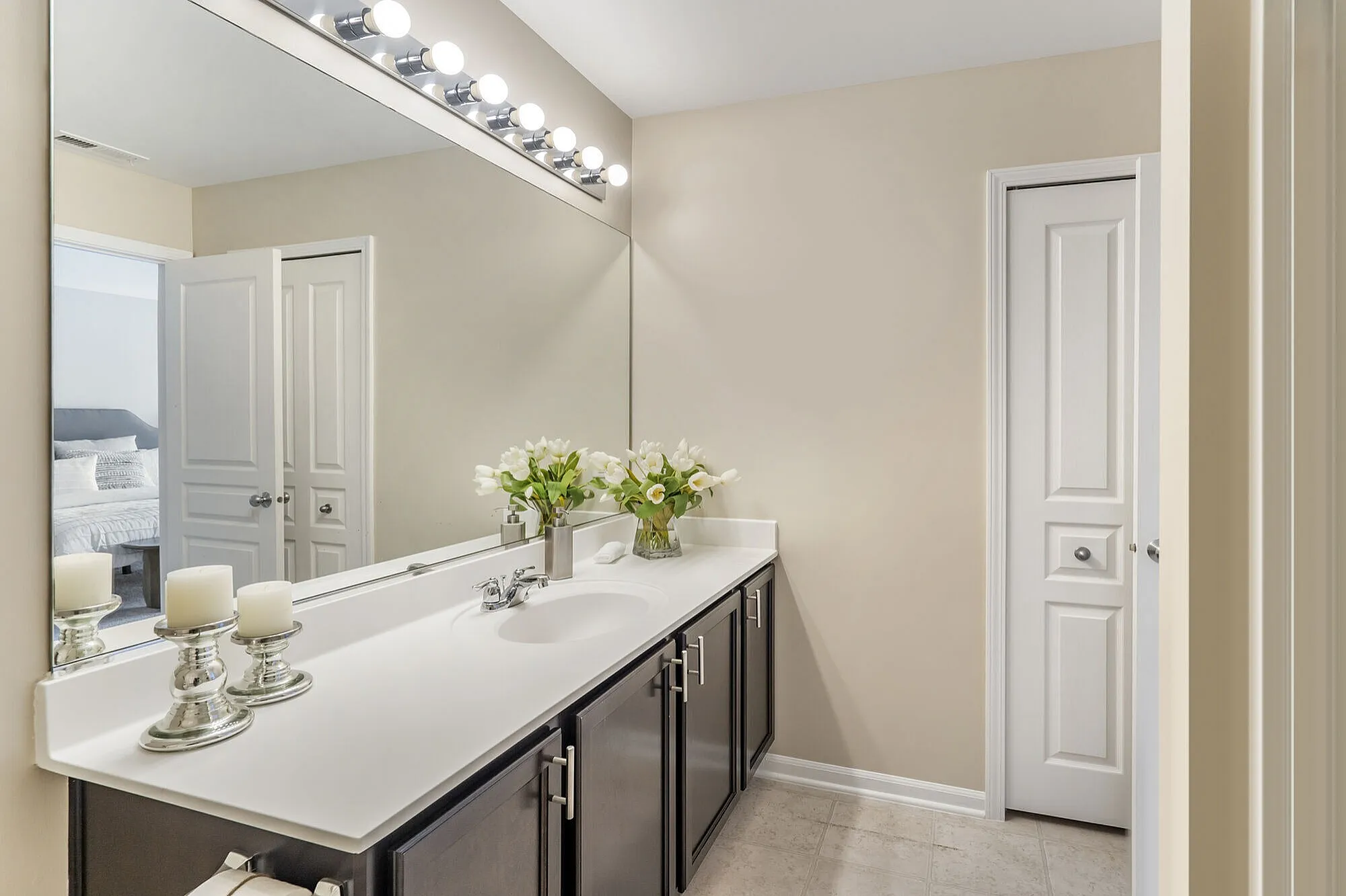 Elegant bathroom with a large mirror, contemporary lighting, a sleek vanity with twin sinks, and stylish floral decor.