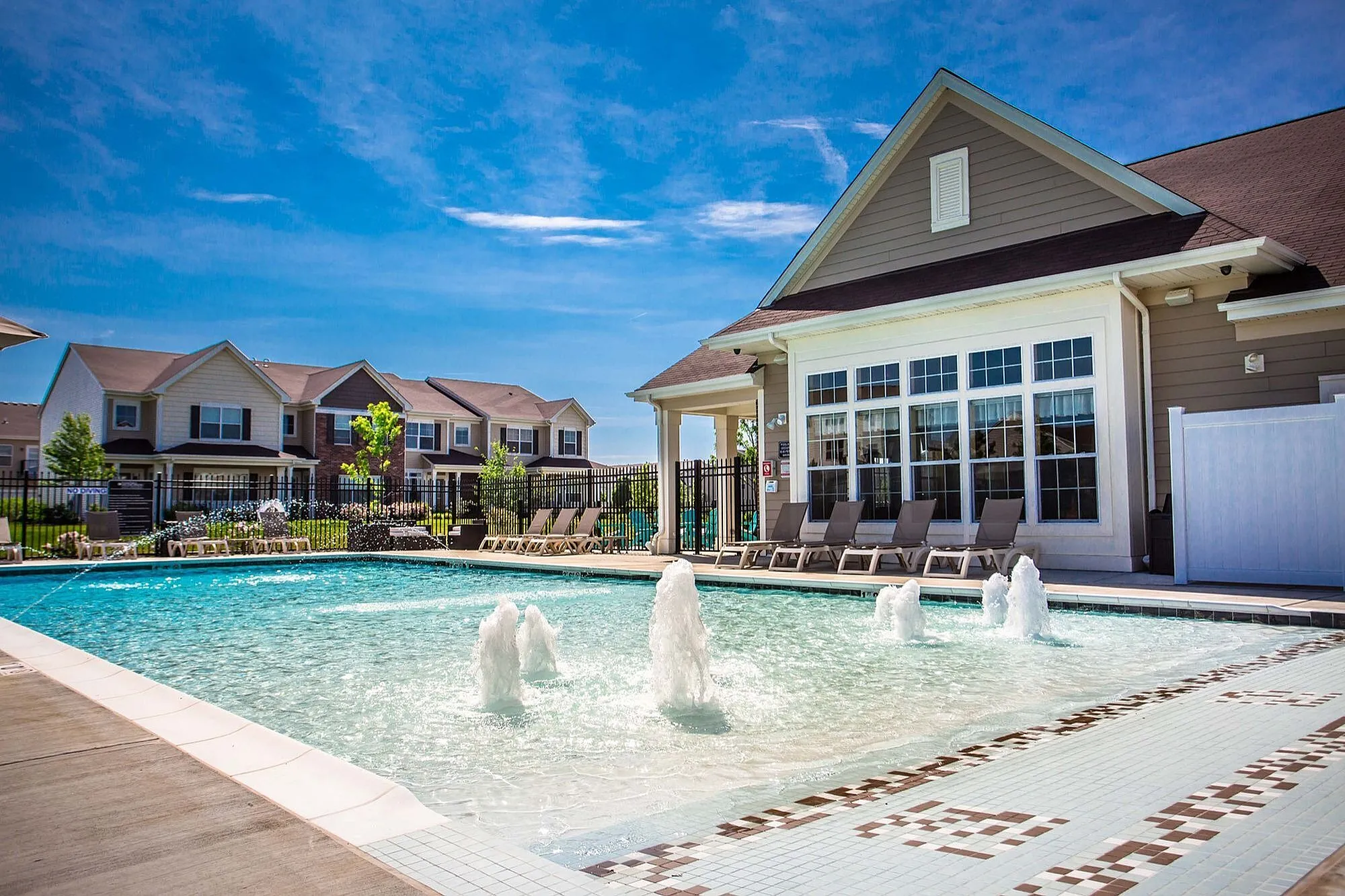 Inviting apartment complex pool area with elegant fountains, surrounded by modern townhouses and sun loungers for a relaxing retreat.