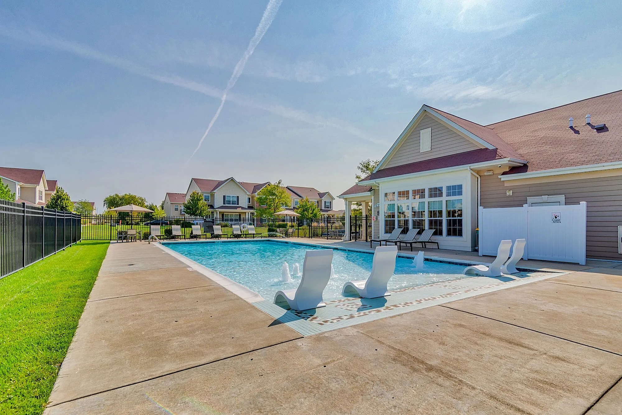 Inviting outdoor pool area with modern lounge chairs and sunny residential backdrop, perfect for relaxation and leisure.