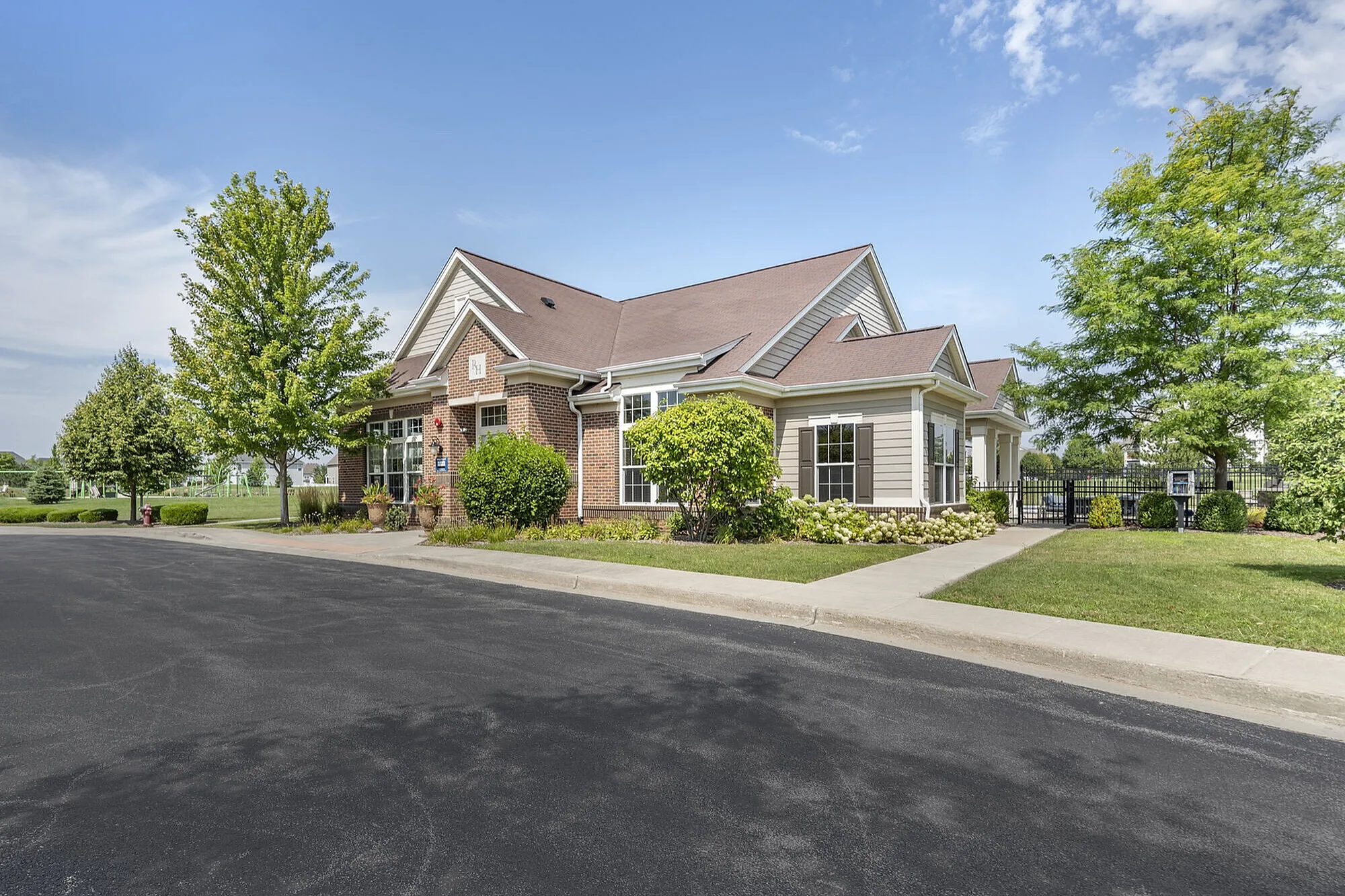 Charming suburban home with a brick exterior, surrounded by lush greenery and a well-maintained landscape under a bright blue sky.