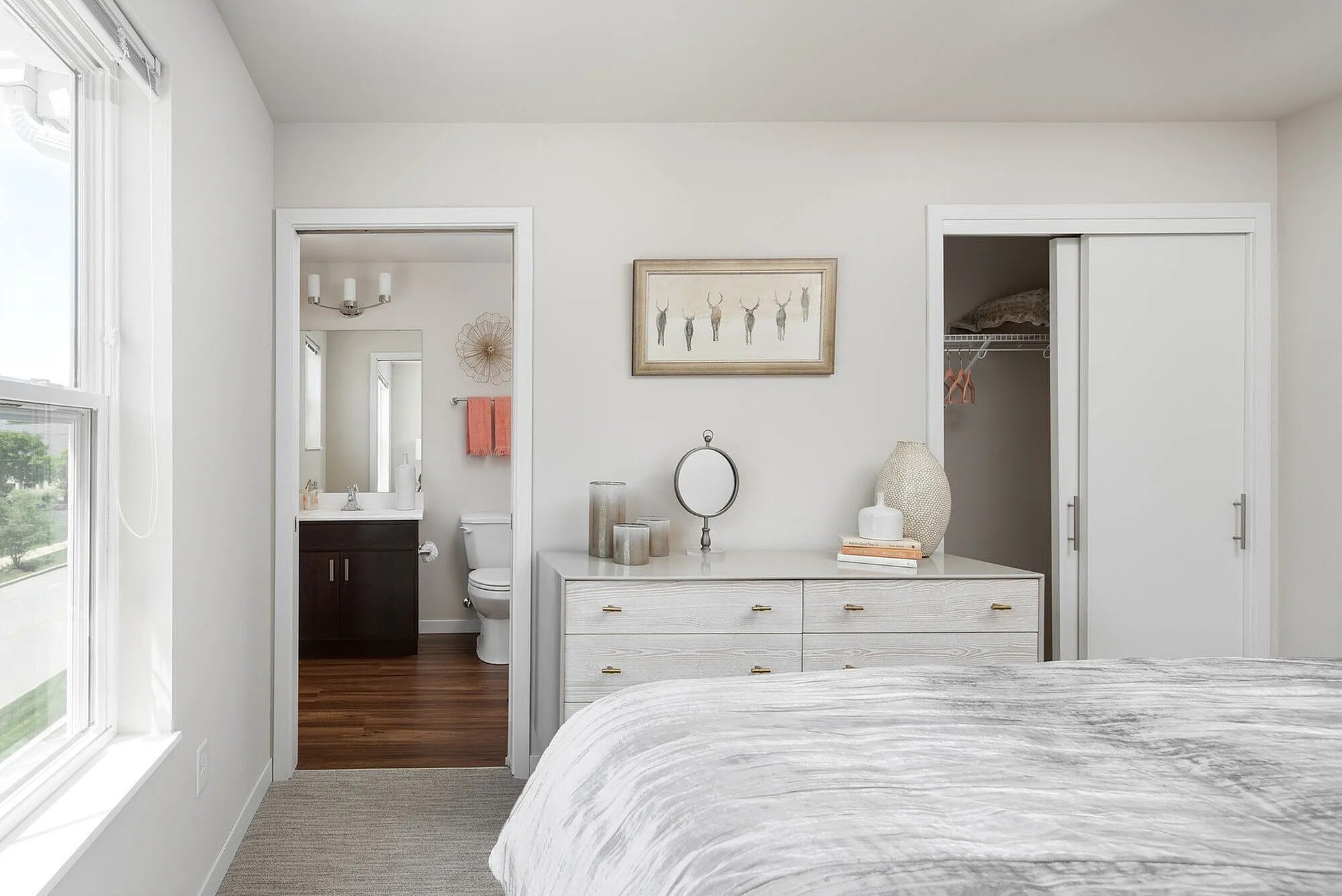 Bright and elegant bedroom with an en-suite bathroom, featuring modern decor and a spacious closet. Natural light floods the room through large windows, creating a serene and inviting atmosphere.