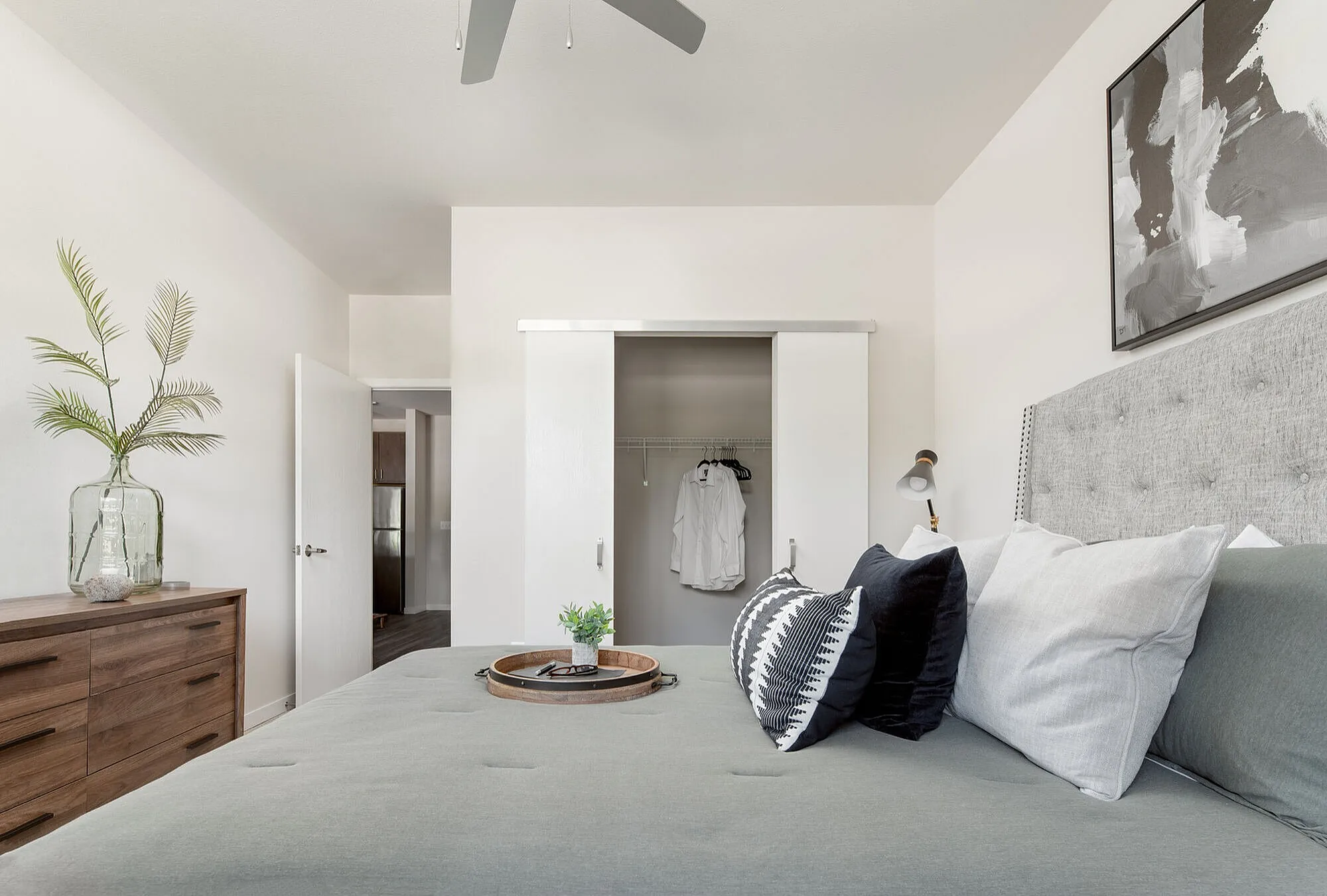 Elegant bedroom with stylish decor featuring a plush gray bed, modern artwork, and a chic wooden dresser with a glass vase.