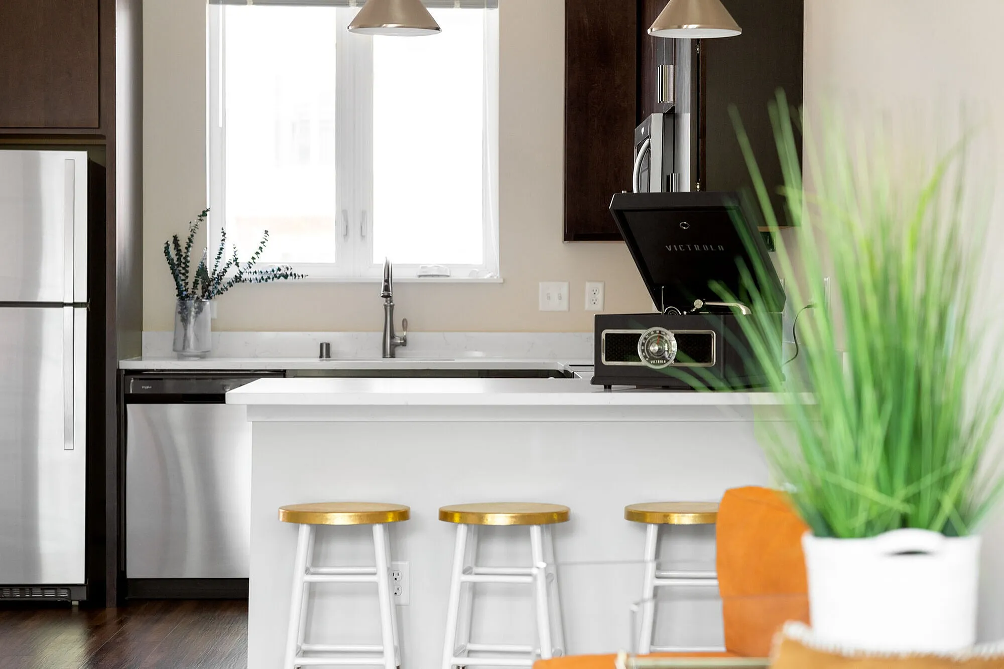 Modern kitchen with sleek stainless steel appliances, white countertops, and stylish barstools, bathed in natural light.