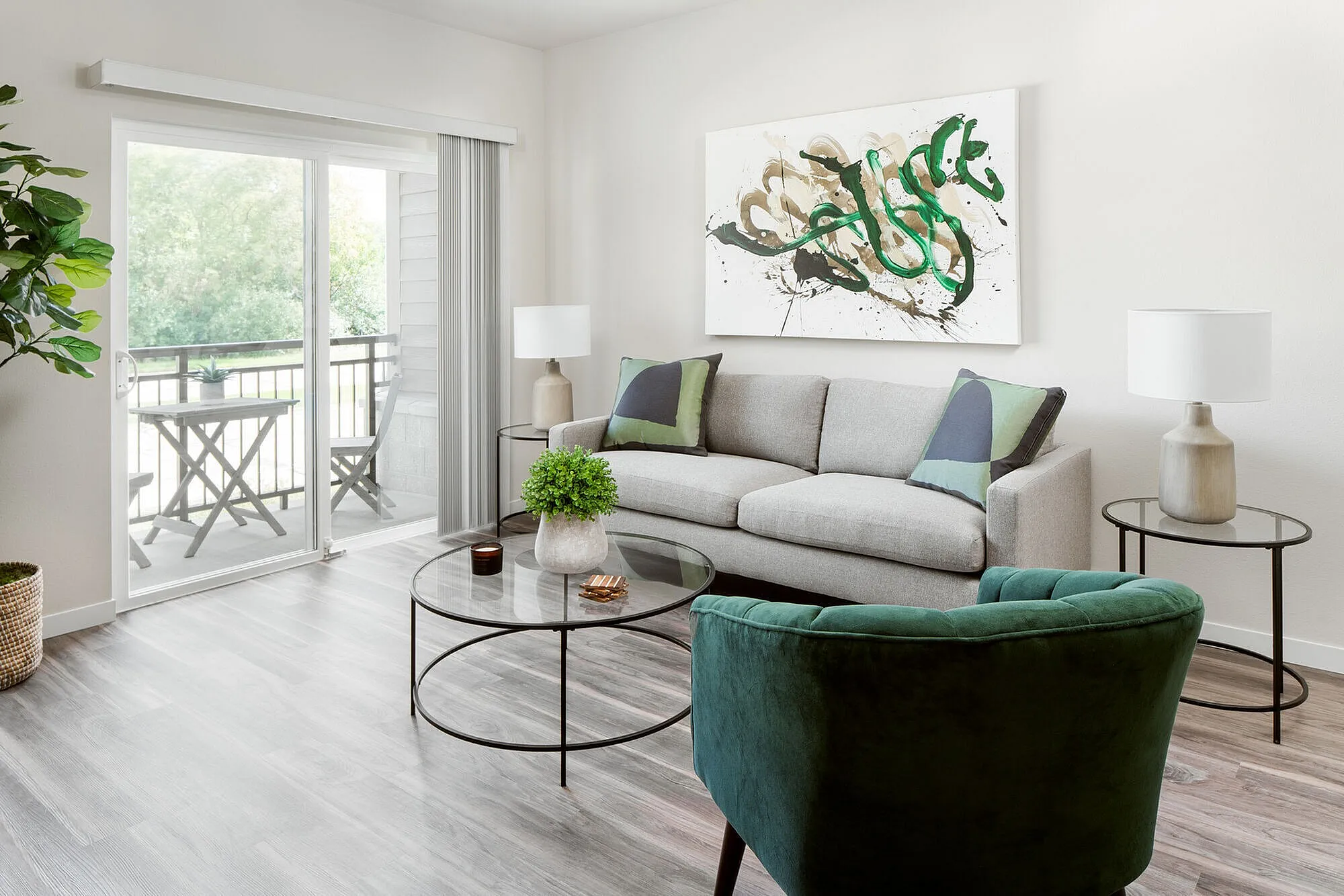 Contemporary living room with stylish décor, featuring a gray sofa, green accent chair, and abstract artwork, leading to a peaceful balcony view.