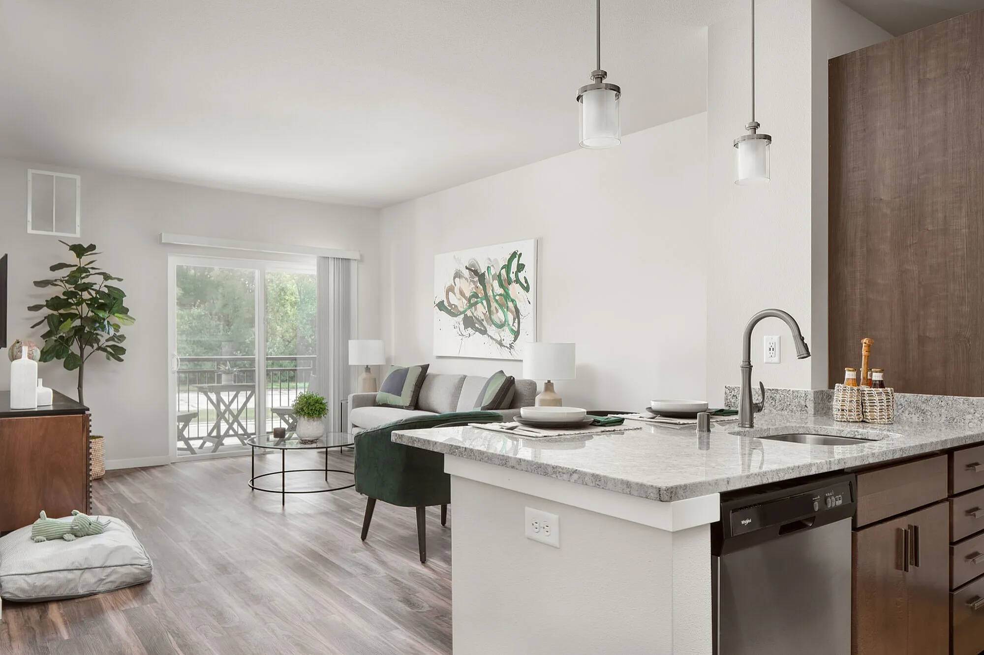 Bright, modern living room and kitchen space featuring sleek granite countertops, stylish pendant lighting, and a cozy, open layout with a view of a lush outdoor area.