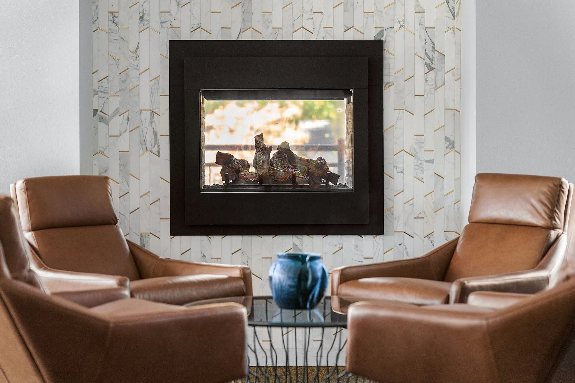 Elegant living space with cozy fireplace, surrounded by stylish marble tiles and modern leather chairs, perfect for relaxation.