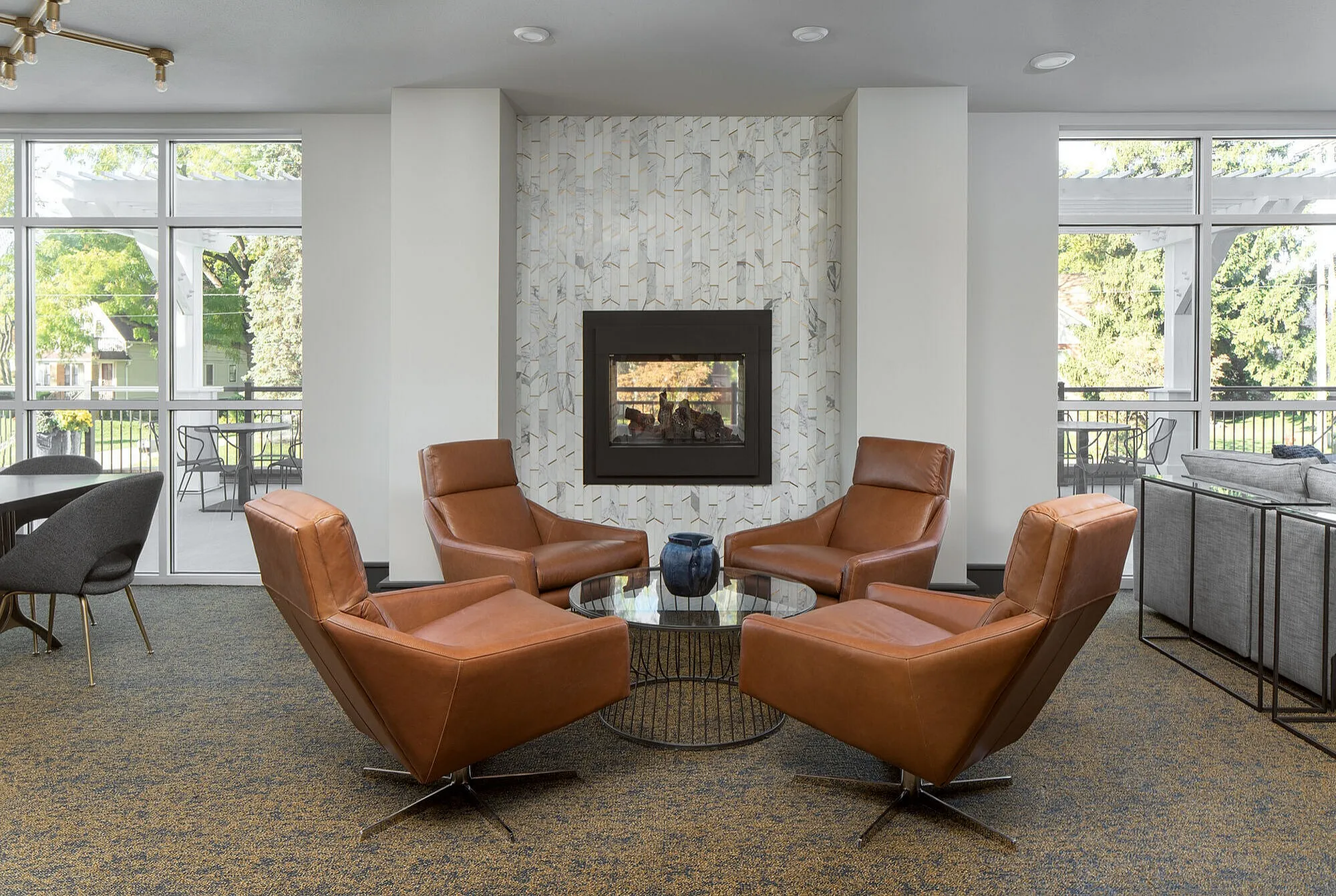 Chic apartment lounge with modern leather armchairs, elegant fireplace, and floor-to-ceiling windows offering lush garden views.