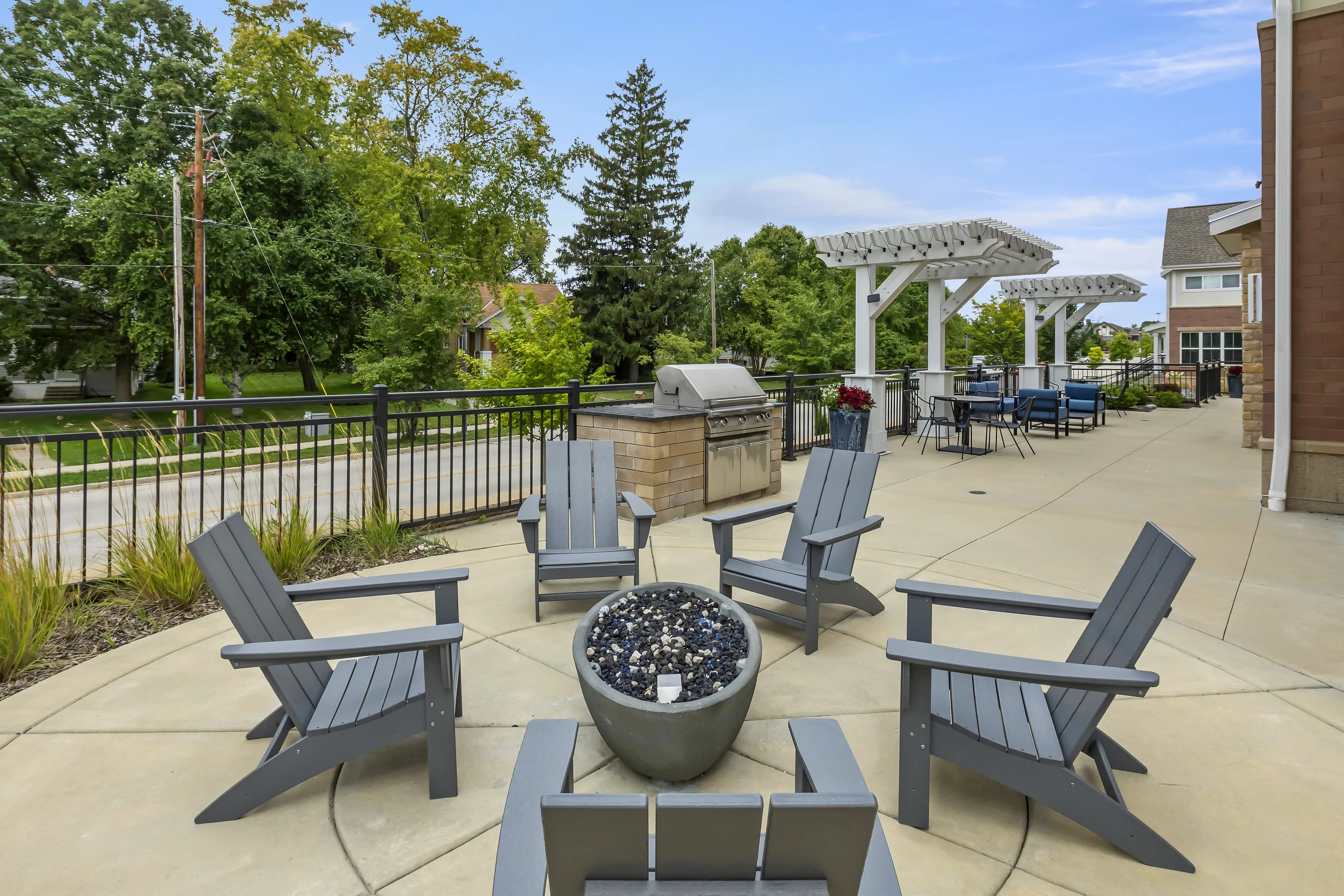 Chic outdoor patio featuring cozy Adirondack chairs around a modern fire pit, perfect for entertaining, with lush greenery and stylish pergola in the background.