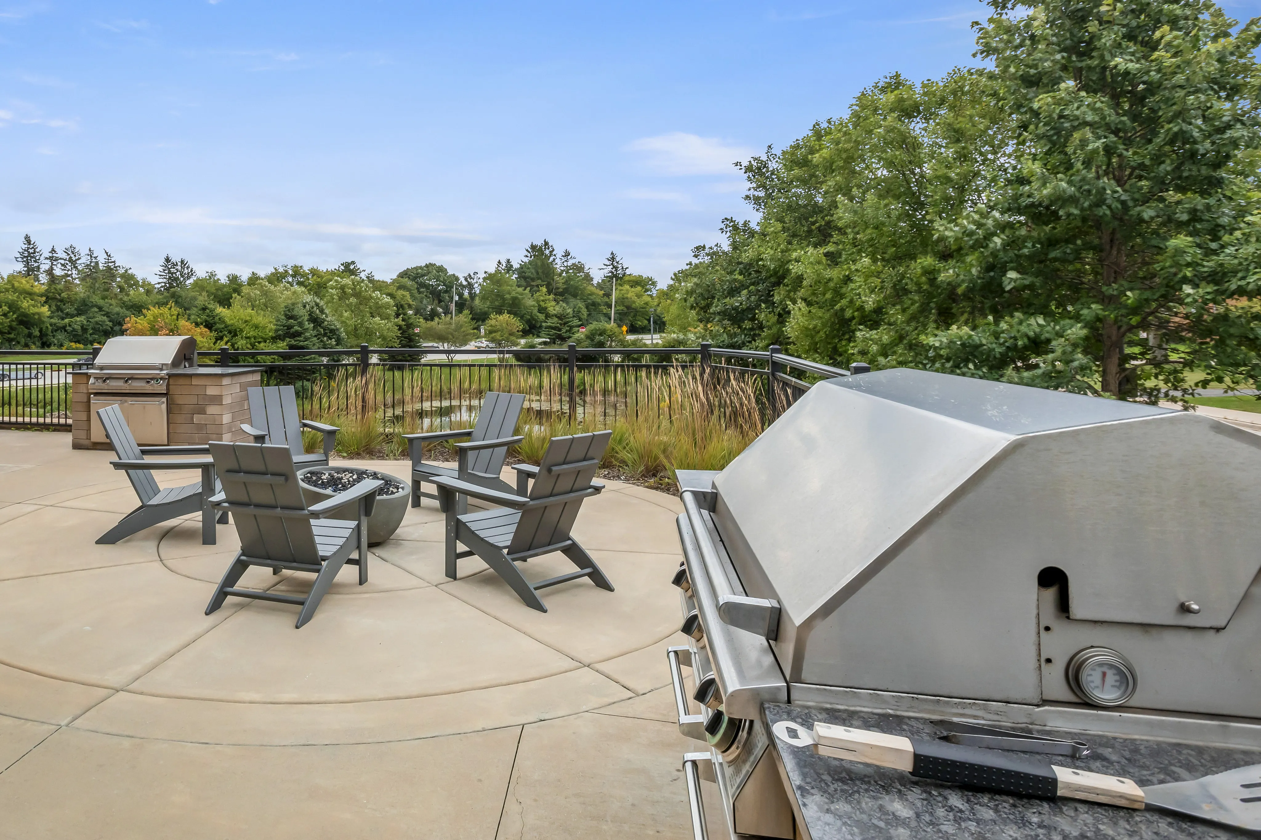 Inviting outdoor patio with modern grill, cozy seating around a fire pit, and lush, green park views.