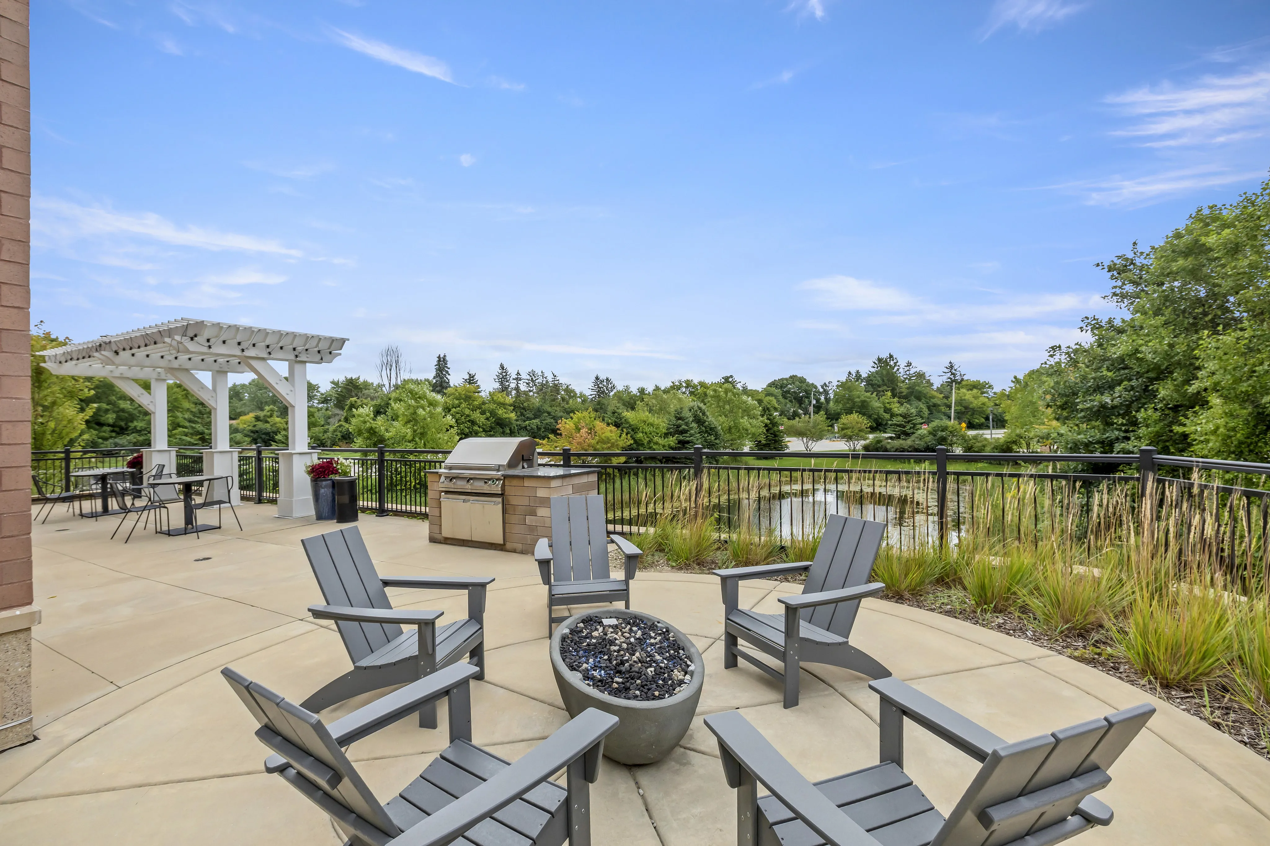 Charming outdoor patio with Adirondack chairs, fire pit, BBQ grill, and pergola, overlooking scenic greenery.