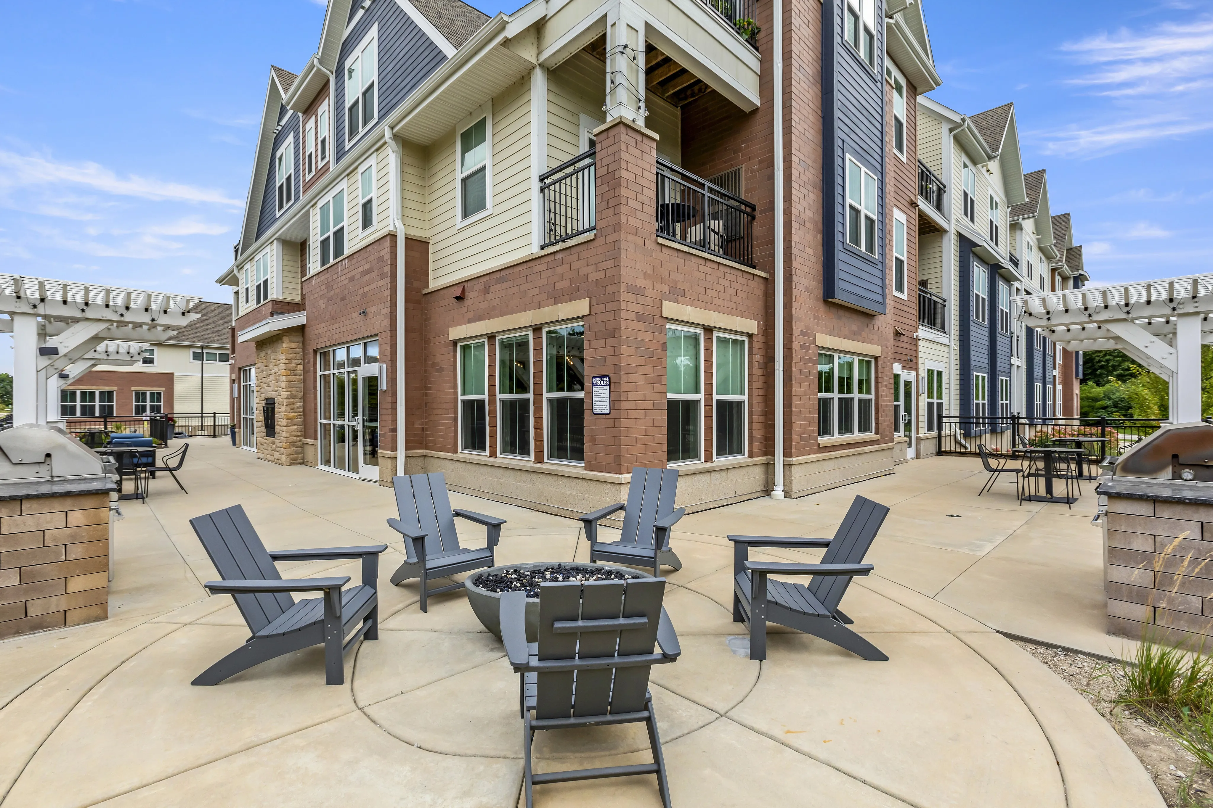 Inviting apartment complex exterior with spacious patio featuring Adirondack chairs and a modern pergola for relaxation.