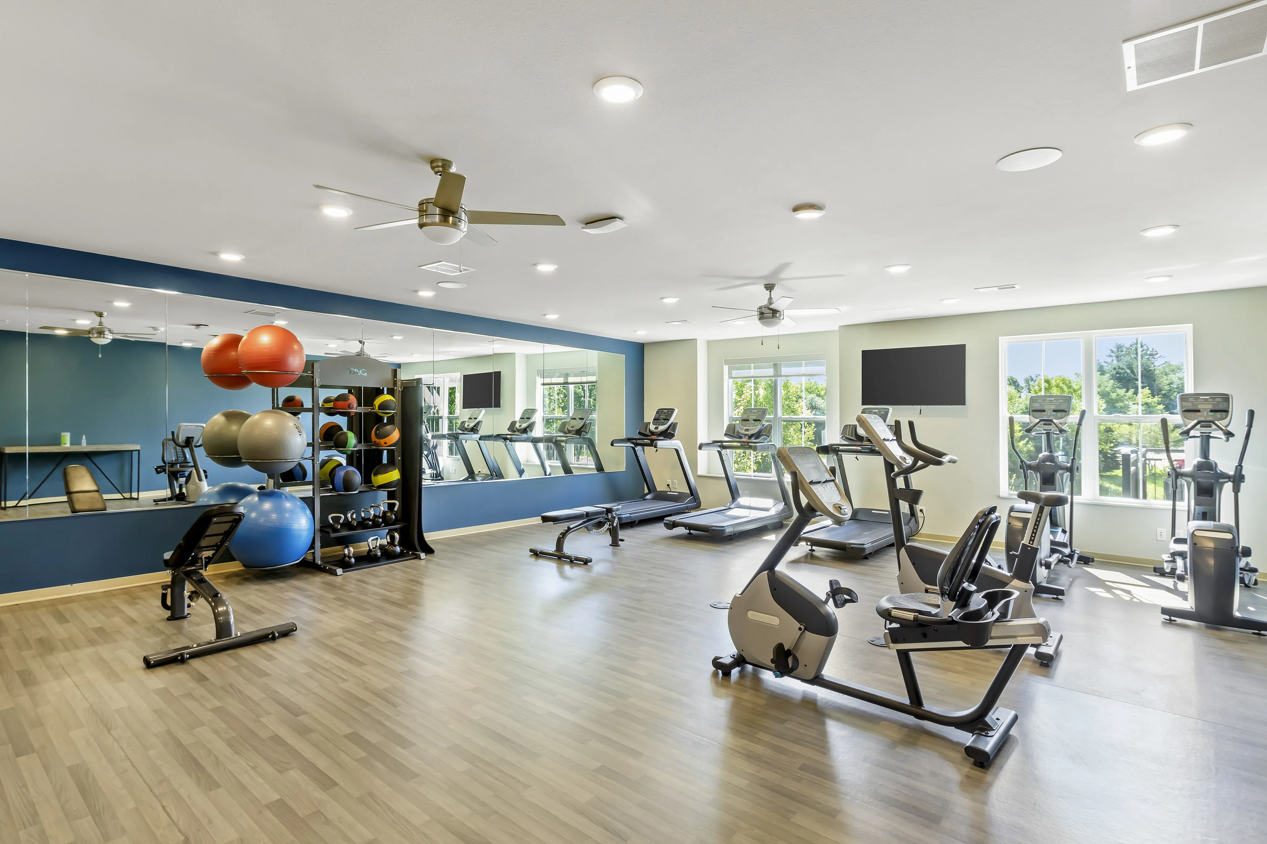 Bright and spacious fitness center with state-of-the-art exercise machines, mirrored walls, and natural light streaming through large windows.