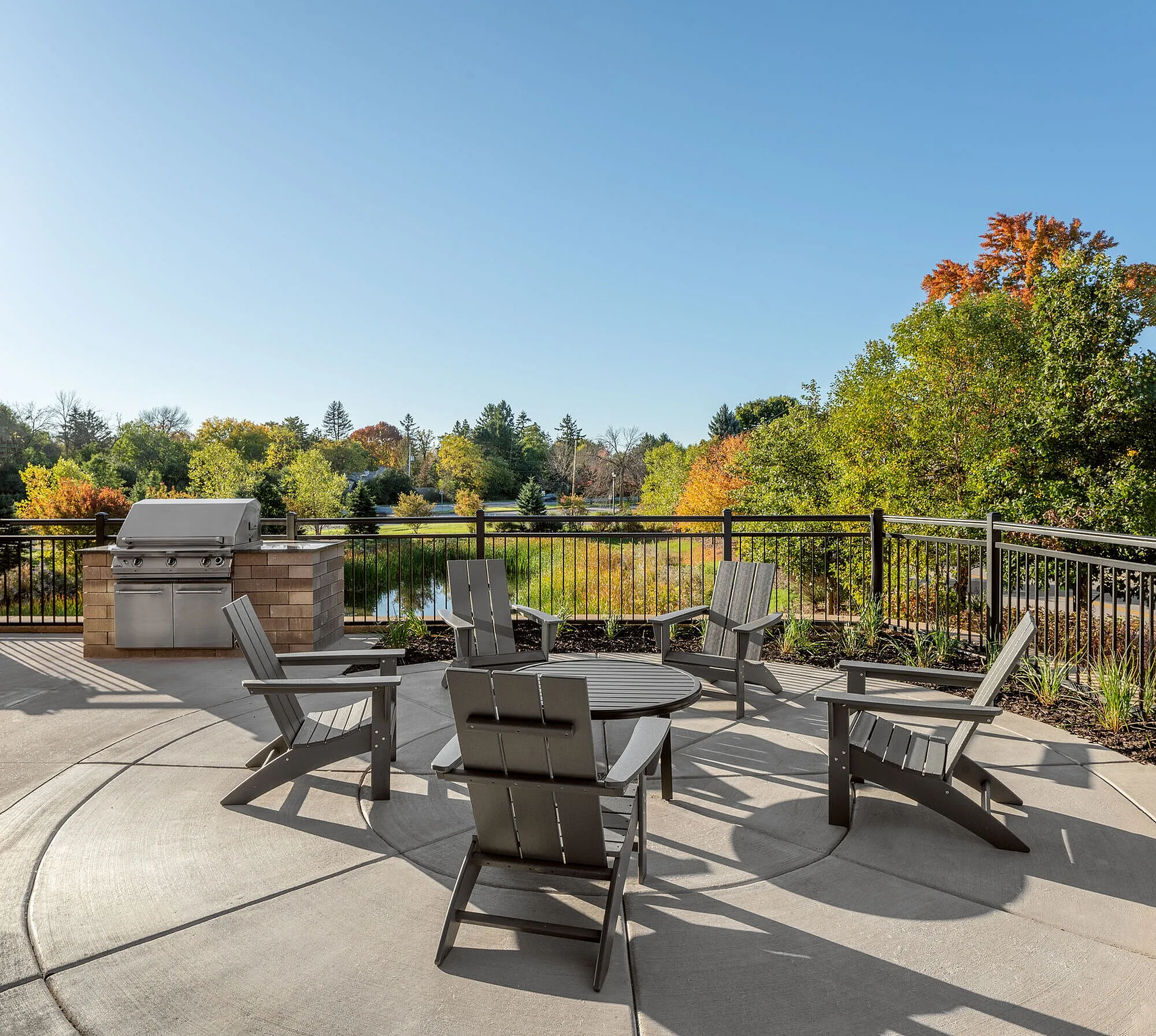 Charming outdoor patio with modern seating, barbecue area, and scenic view of lush greenery and colorful autumn trees.