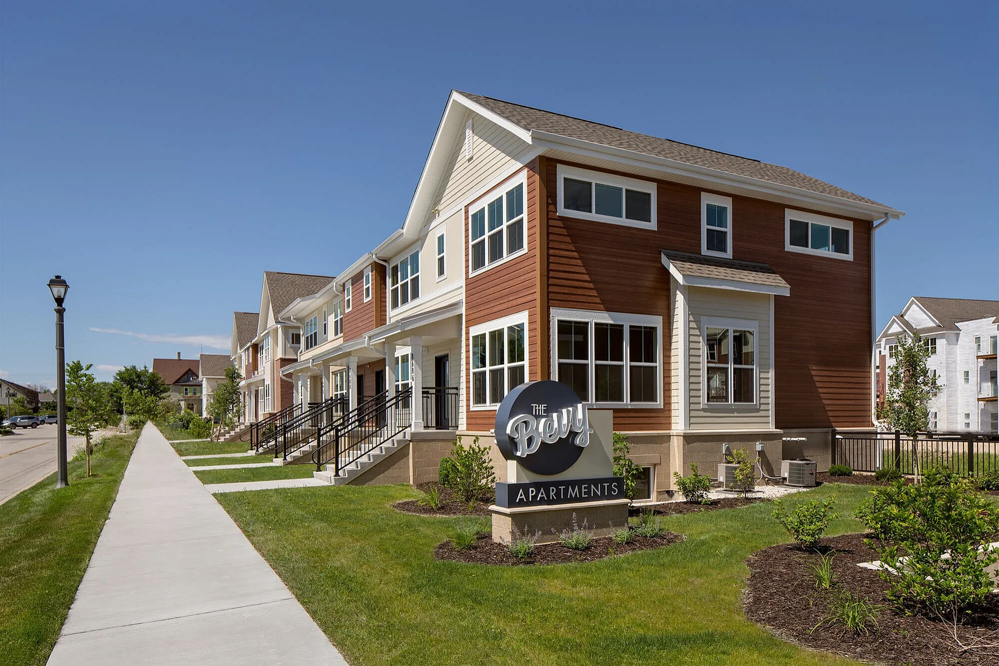 Charming exterior view of The Betty Apartments showcasing modern townhouses with inviting entryways and well-maintained landscaping on a sunny day.