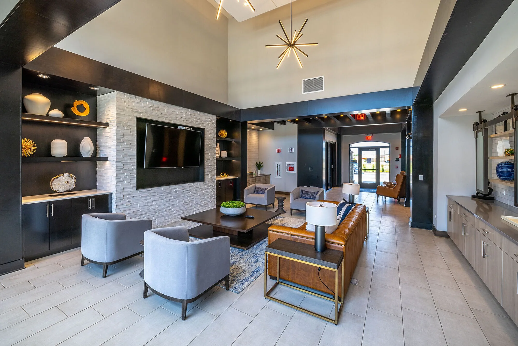 Elegant modern lobby featuring a sleek design with plush seating, decorative shelving, and a large TV, capturing a welcoming and stylish atmosphere.