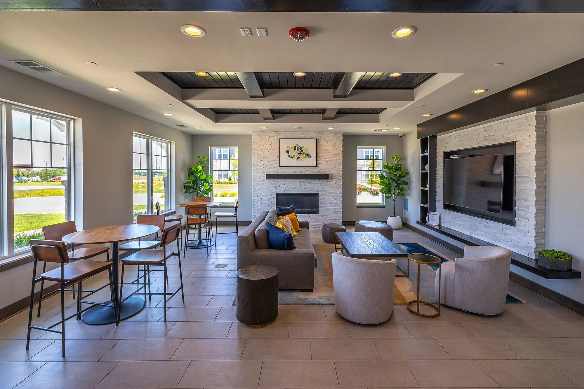 Bright and modern lounge area featuring stylish seating, a cozy fireplace, large flat-screen TV, and abundant natural light from surrounding windows.
