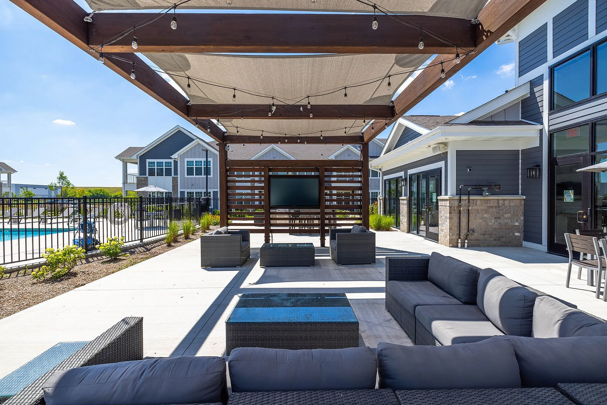 Elegant outdoor lounge area with modern sofas under a stylish pergola overlooking a refreshing pool, perfect for relaxation and entertainment.