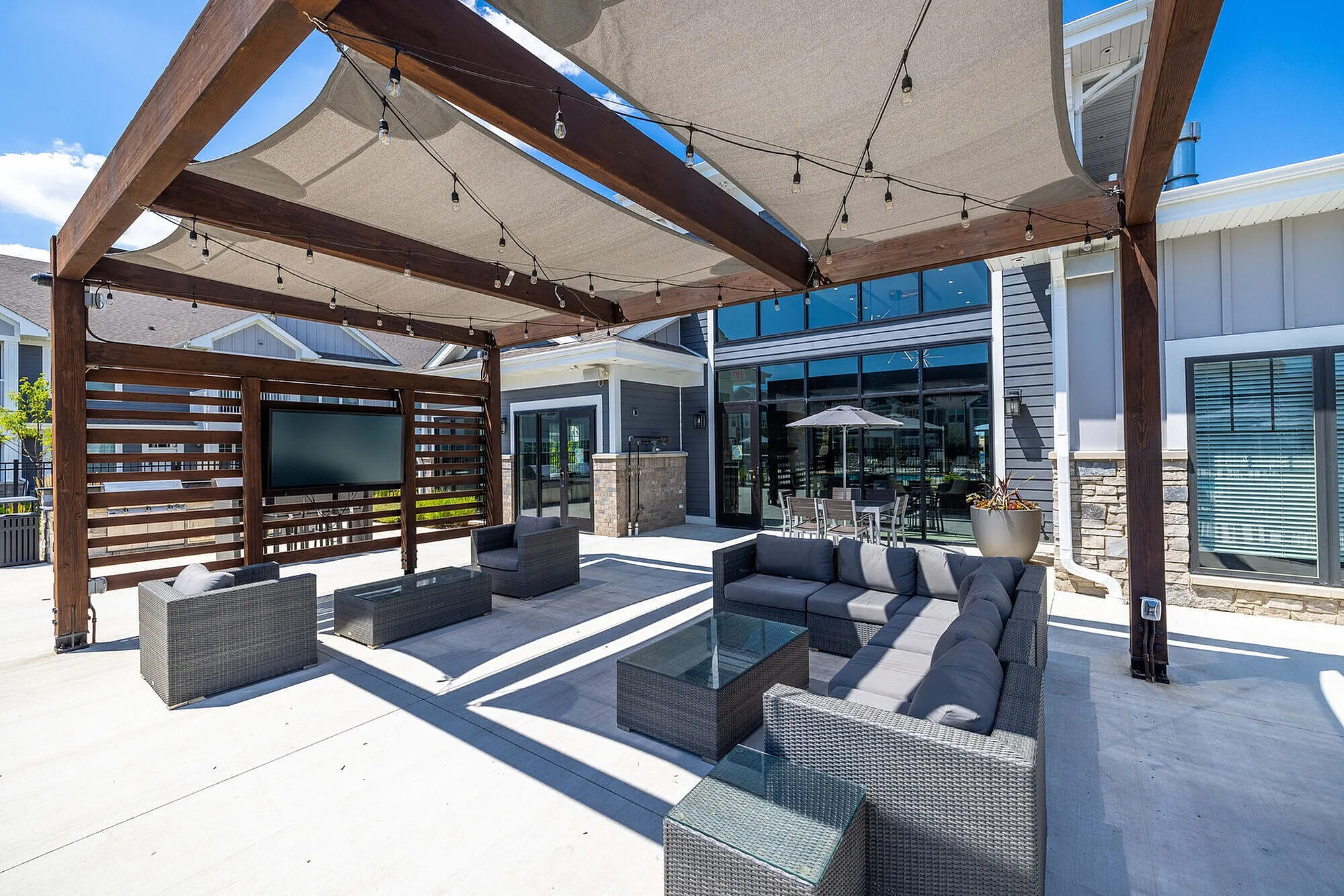 Modern outdoor lounge with stylish gray wicker seating, a pergola with integrated lighting, and contemporary decor features.