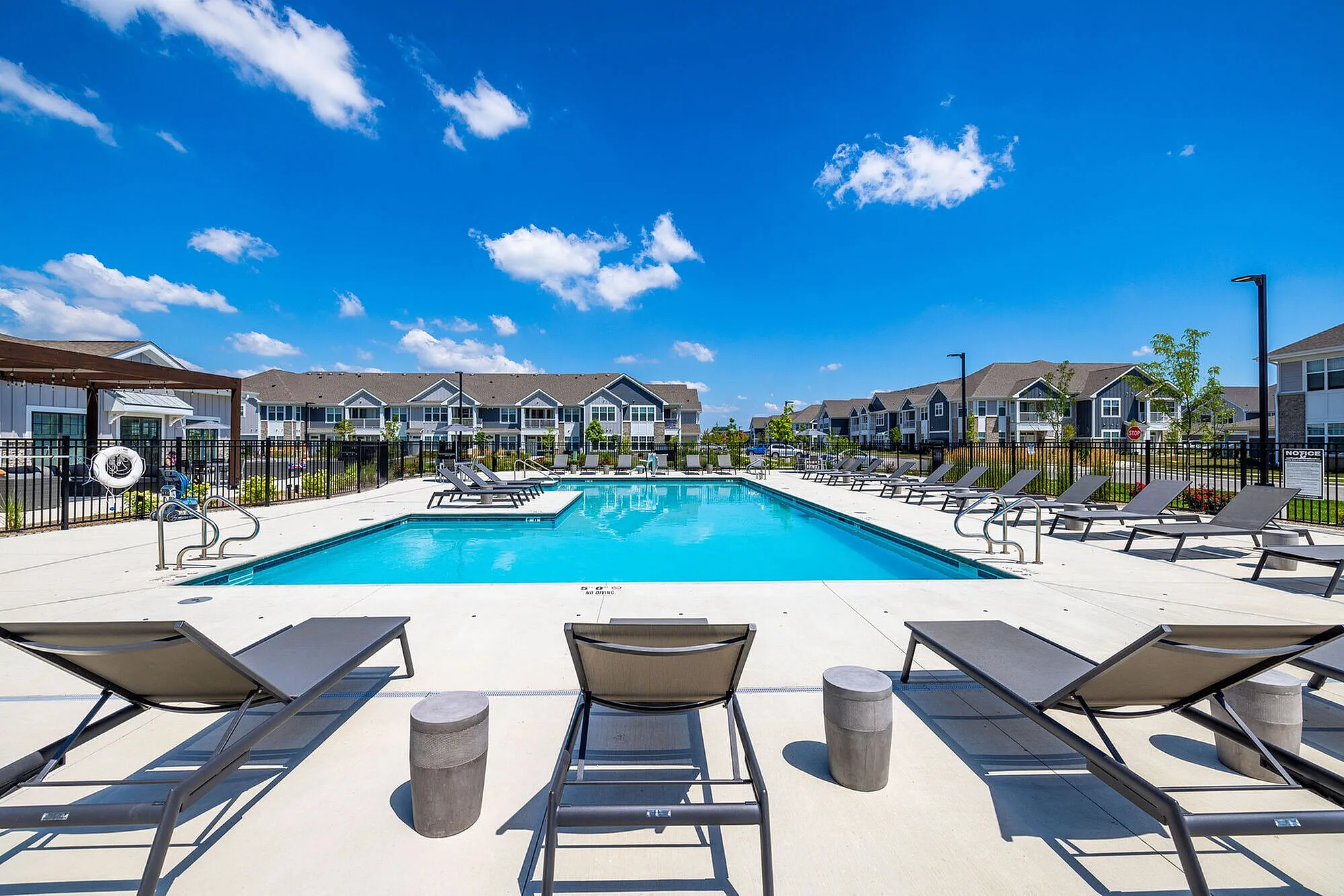Inviting outdoor pool area with stylish lounge chairs, surrounded by modern apartment buildings under a bright blue sky.