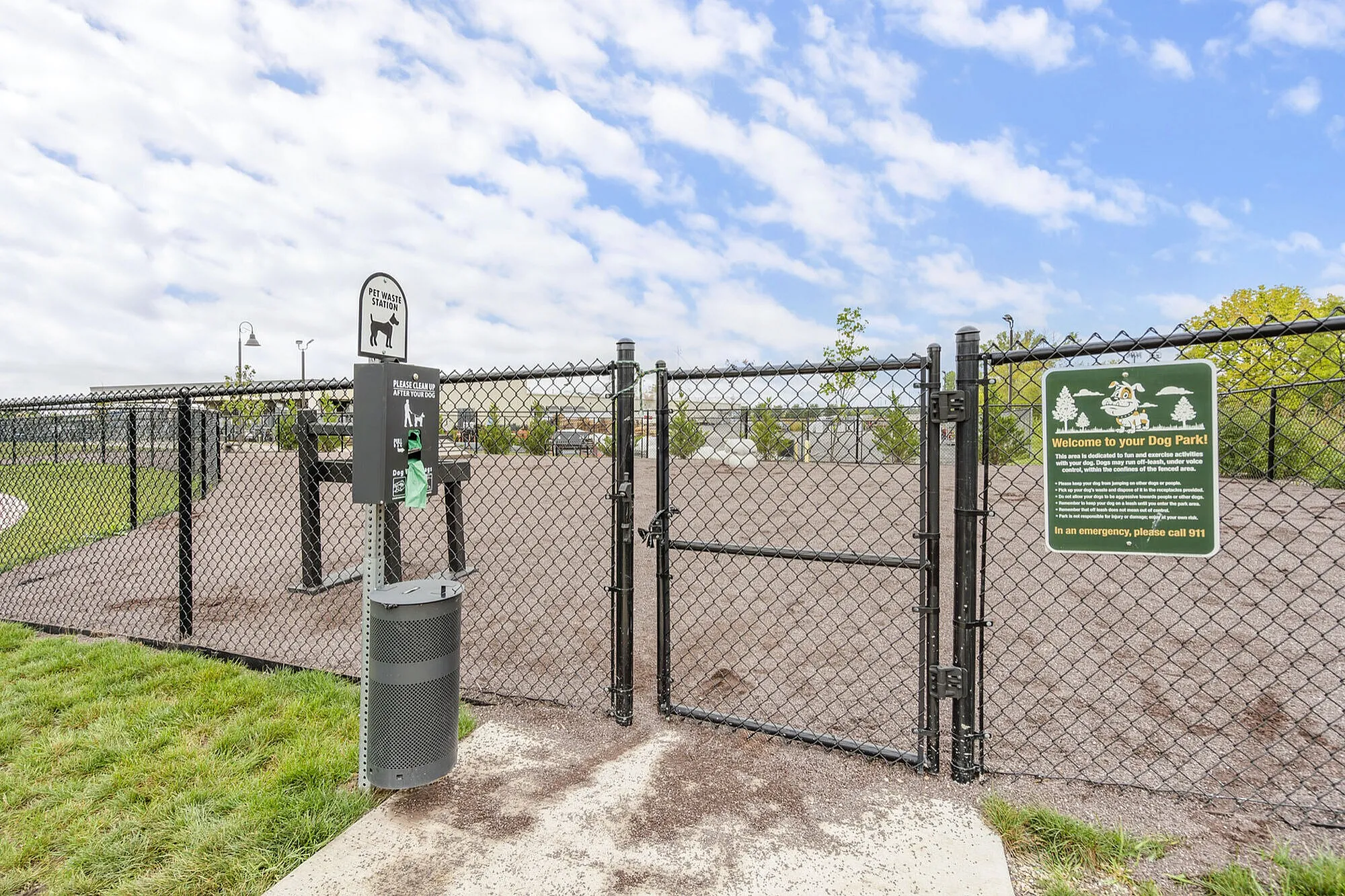 Charming fenced dog park with lush green grass and a pet waste station under a bright blue sky, perfect for pet-friendly apartment living.