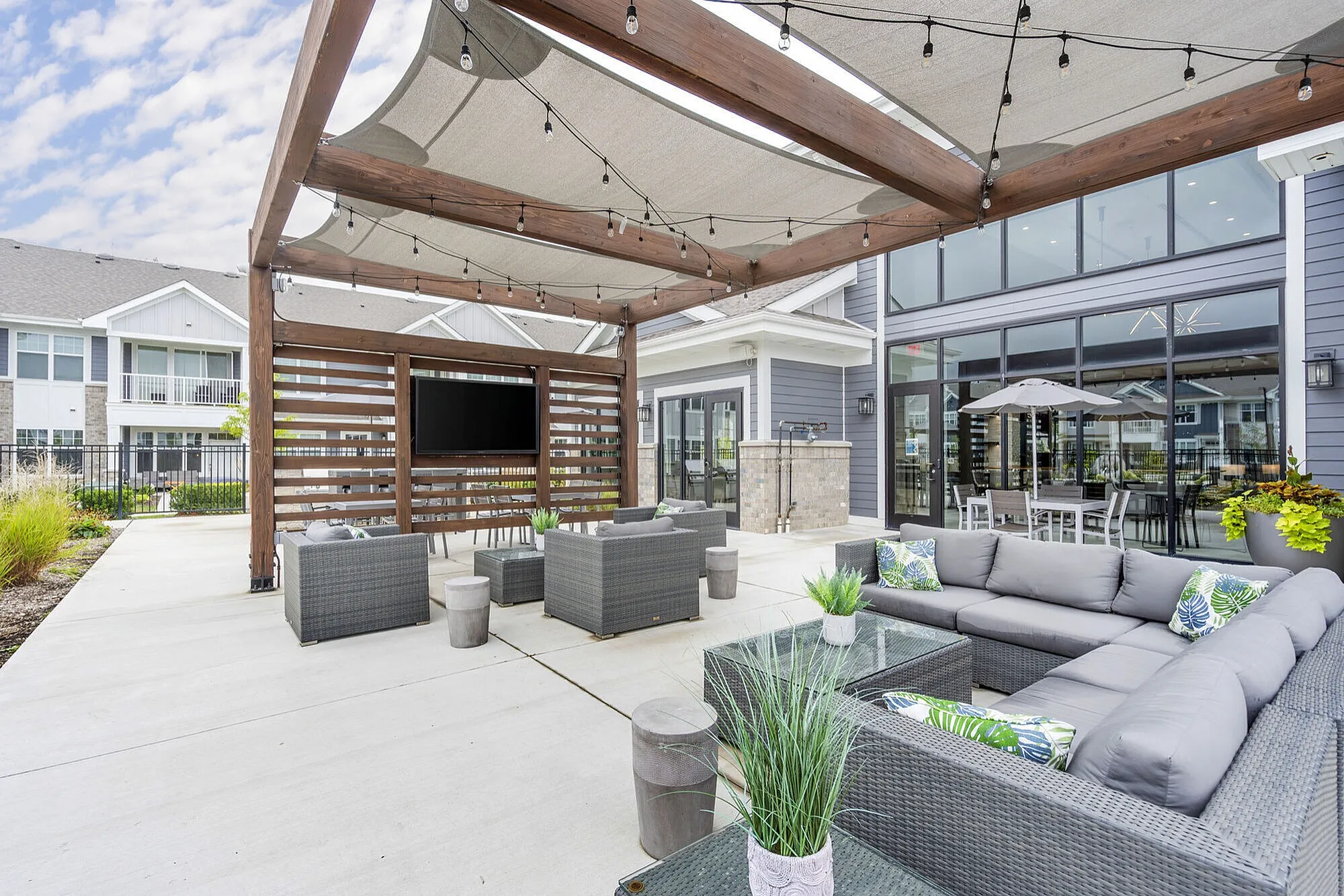 Chic outdoor lounge area with modern wicker furniture, cozy cushions, and a pergola with string lights, perfect for relaxing and social gatherings.