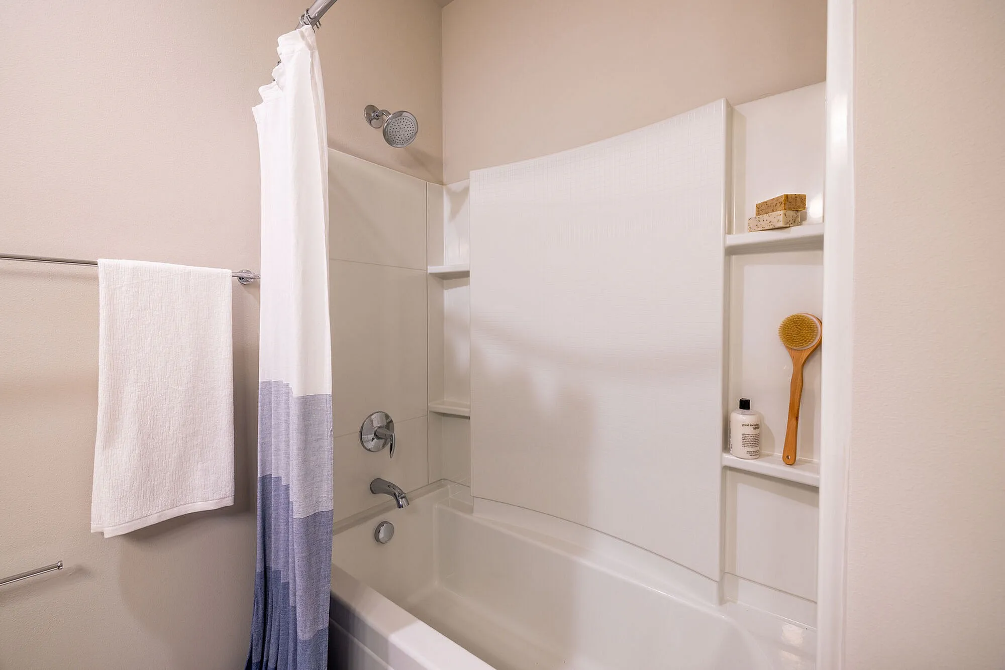 Elegant bathroom featuring a pristine white shower-tub combo, modern fixtures, and stylish shelving for toiletries.