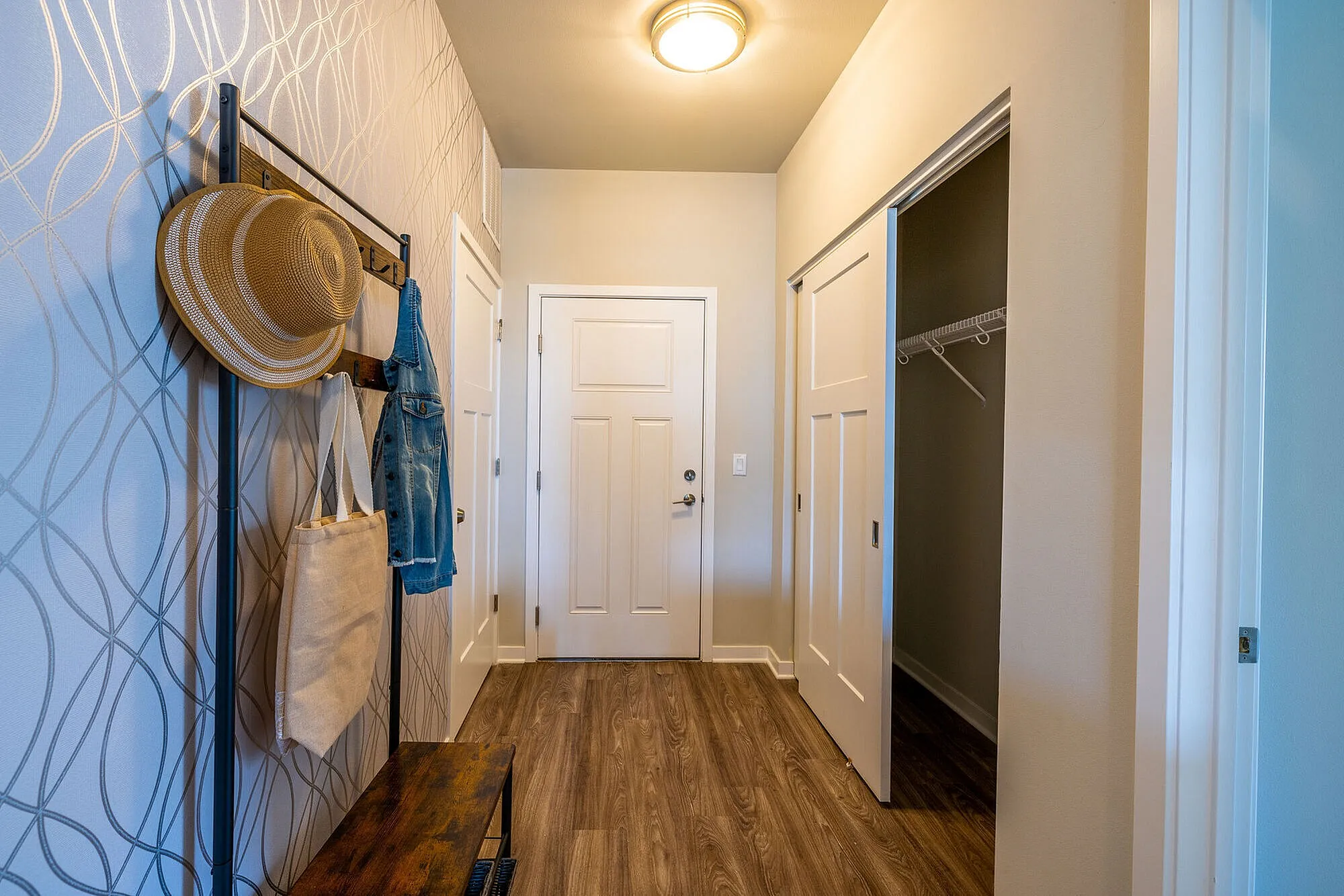 Inviting apartment entryway with chic wallpaper, stylish hat rack, and spacious closet.