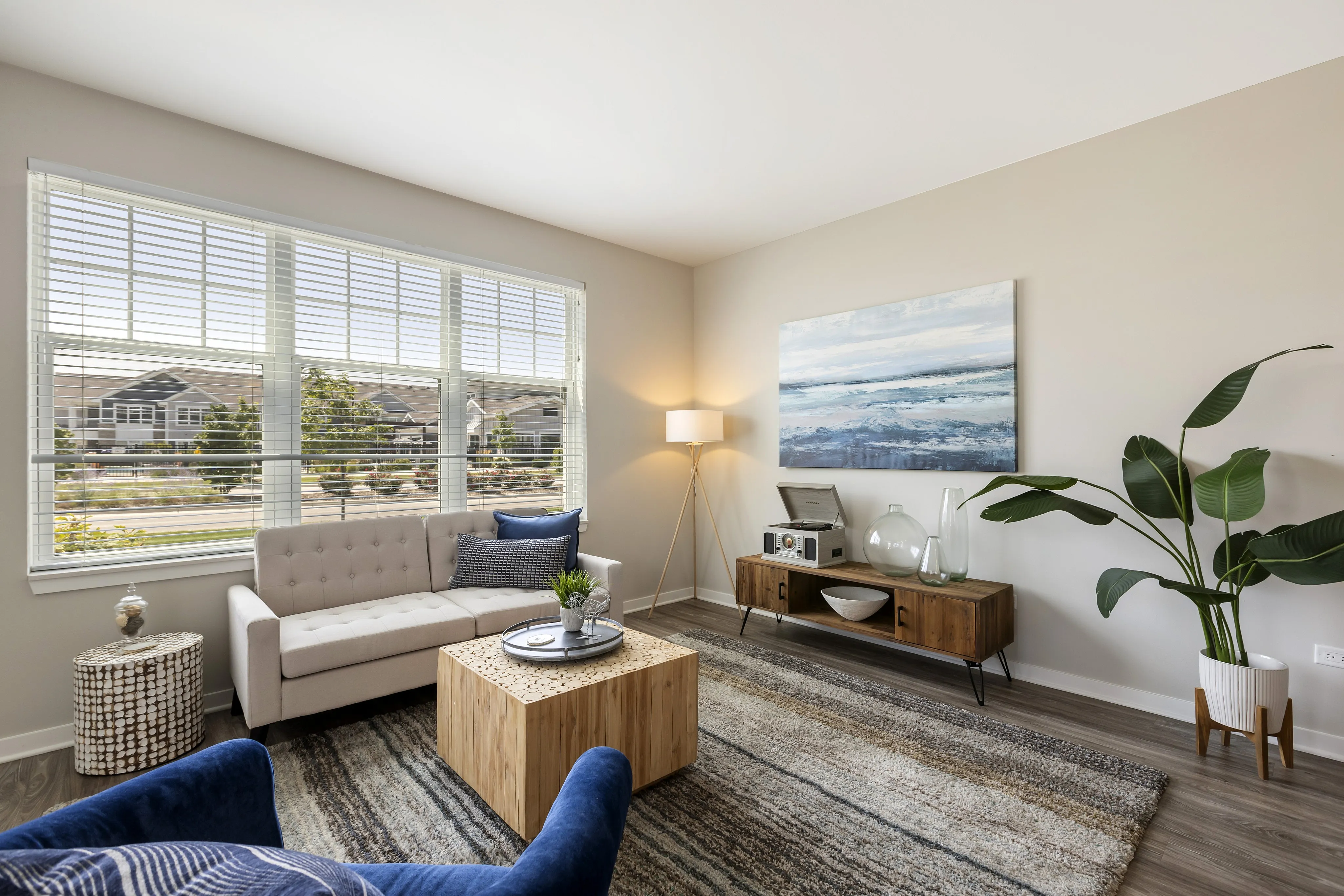 Bright and inviting living room with large windows, modern decor, and cozy seating accented by a lush indoor plant.