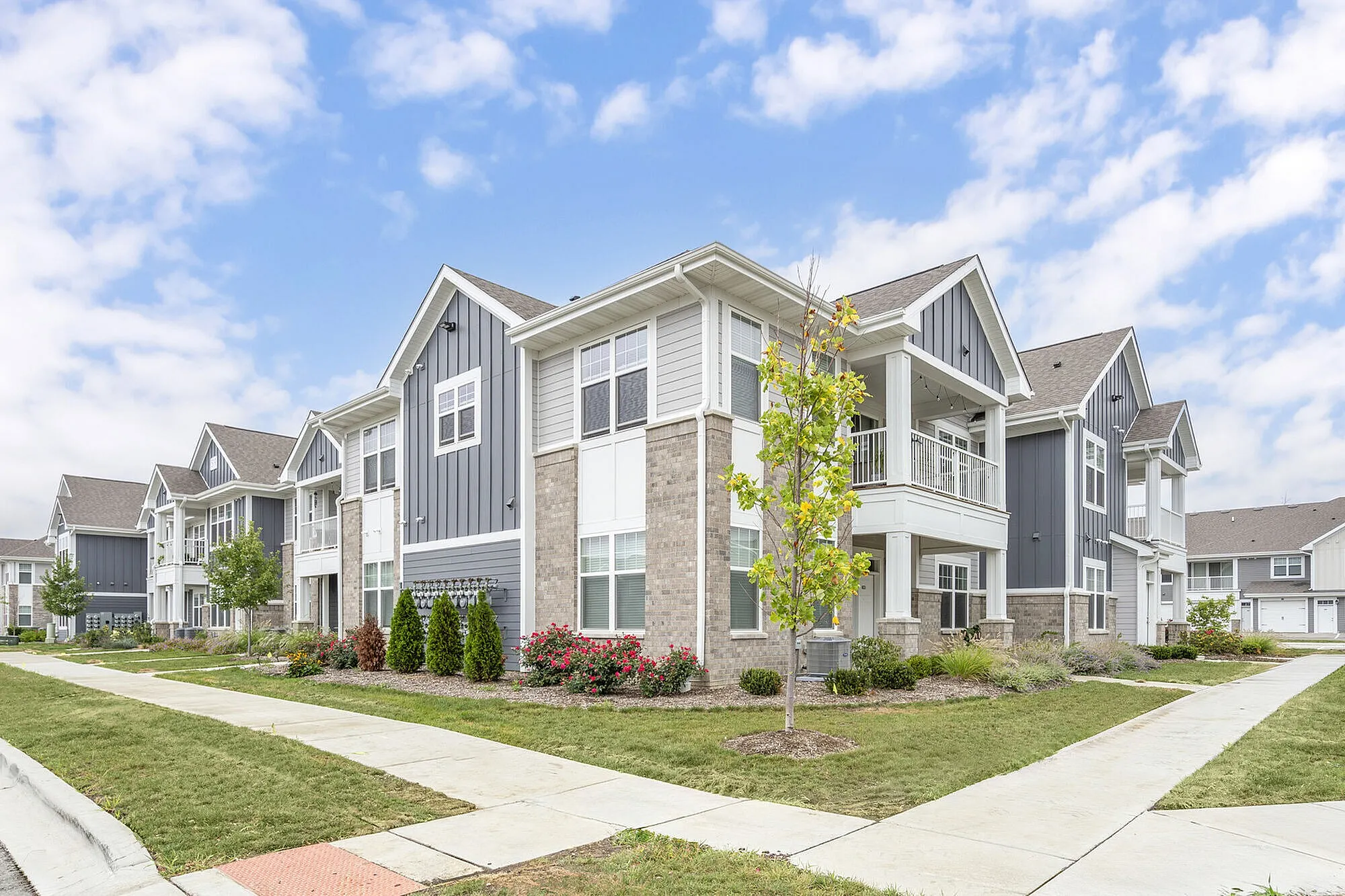 Bright and inviting apartment complex featuring charming gray facades and lush landscaping under a clear blue sky.
