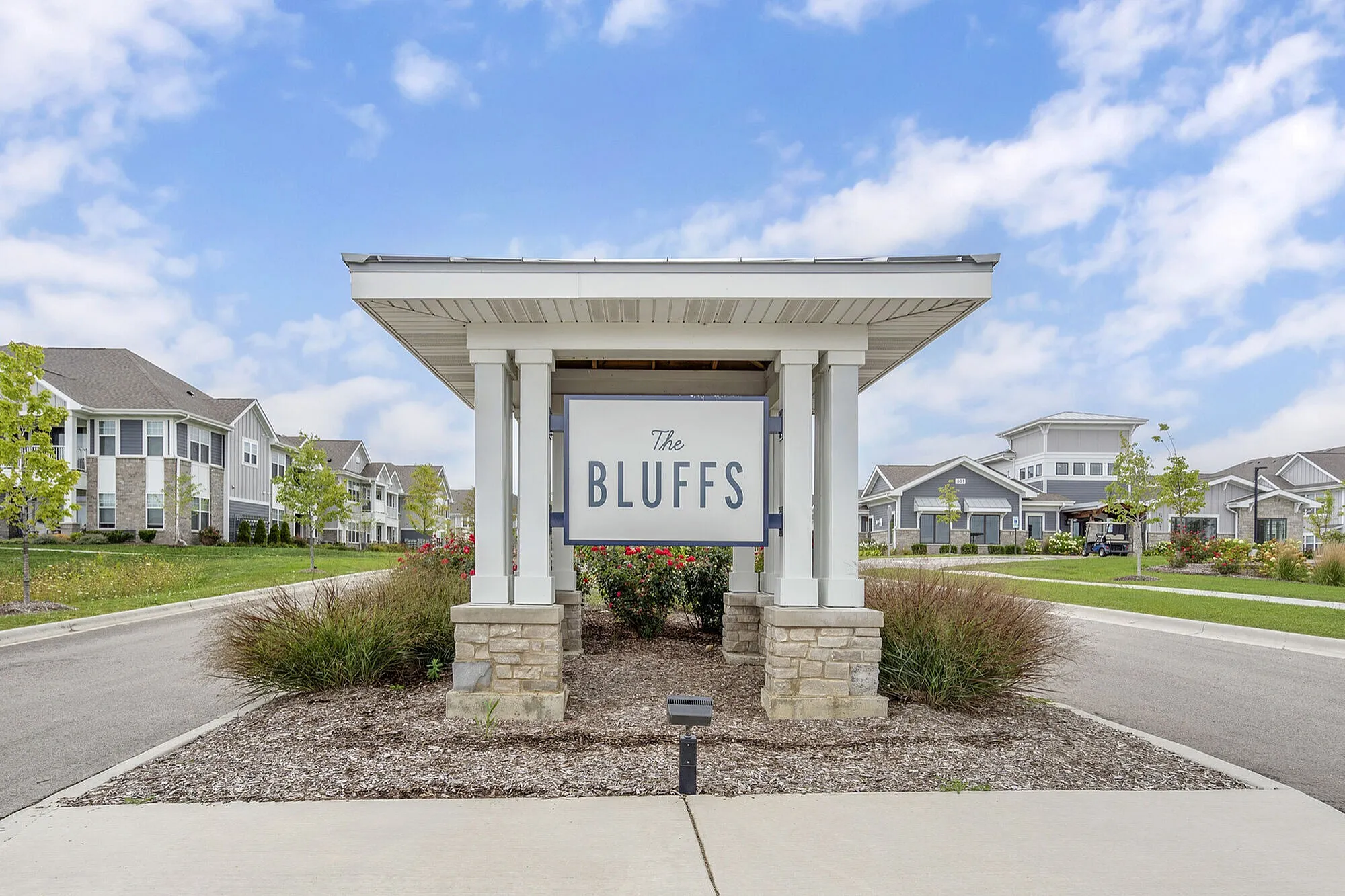 Inviting entrance to The Bluffs apartment community, featuring charming landscaping and modern architecture under a bright blue sky.