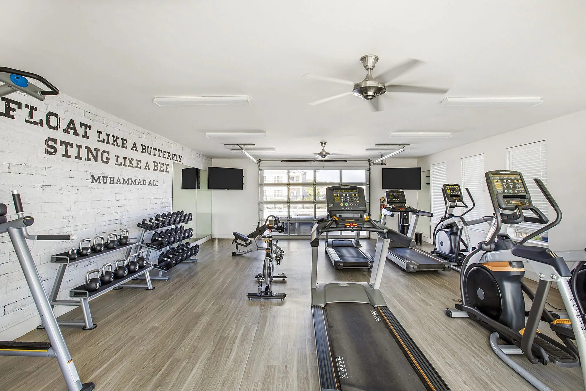 Modern fitness center with state-of-the-art treadmills, stationary bike, and a variety of free weights, accented by a motivational quote on the wall.