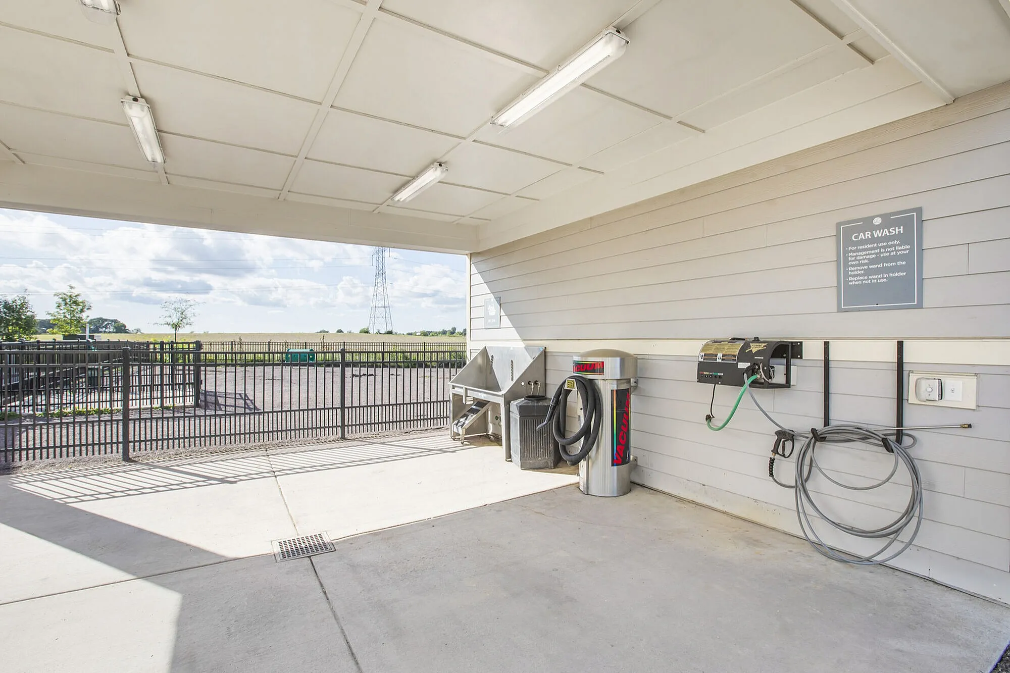 Modern outdoor car wash station with vacuum and hose facilities, featuring open landscape views under a bright sky.