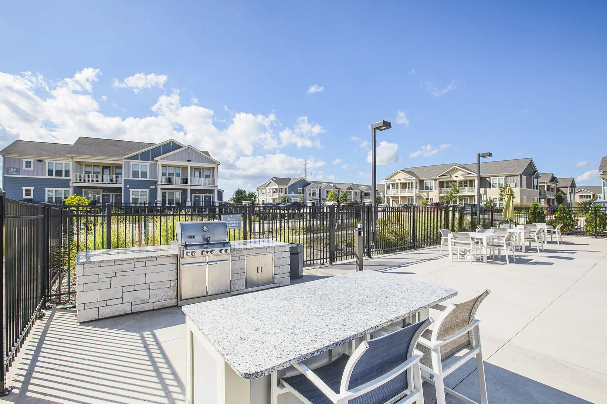 Bright and inviting apartment complex with modern outdoor barbecue area, perfect for entertaining, set against a backdrop of clear blue skies.