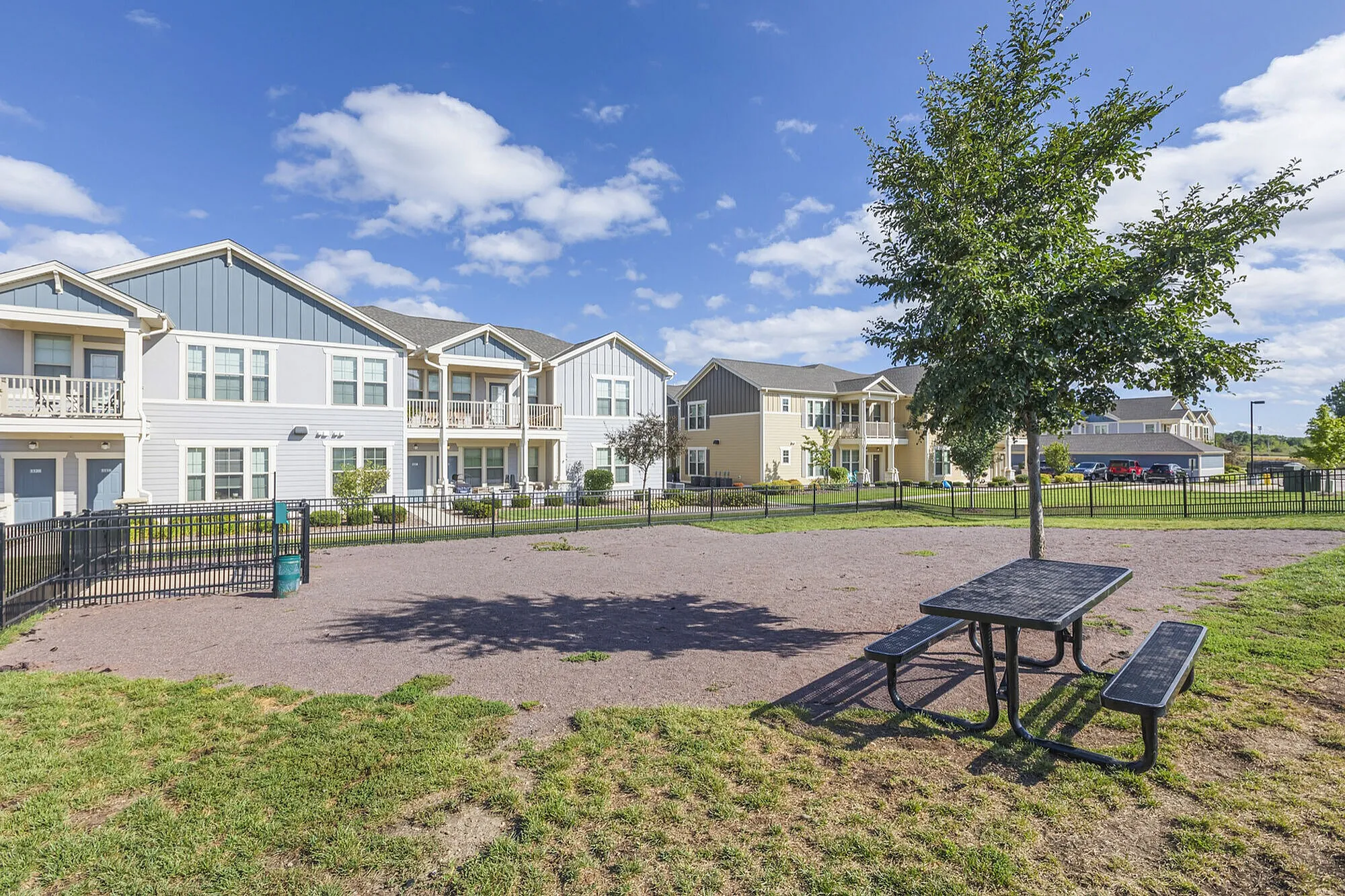 Charming residential community with modern apartments, manicured lawns, and a welcoming park area under a sunny sky.