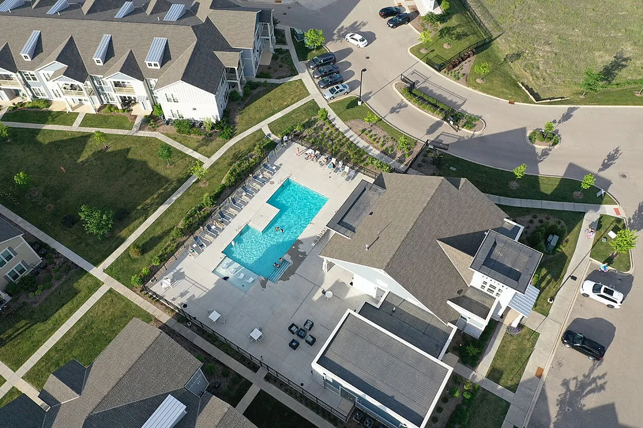 Aerial view of a modern apartment complex with a central swimming pool, surrounded by greenery and well-maintained pathways.