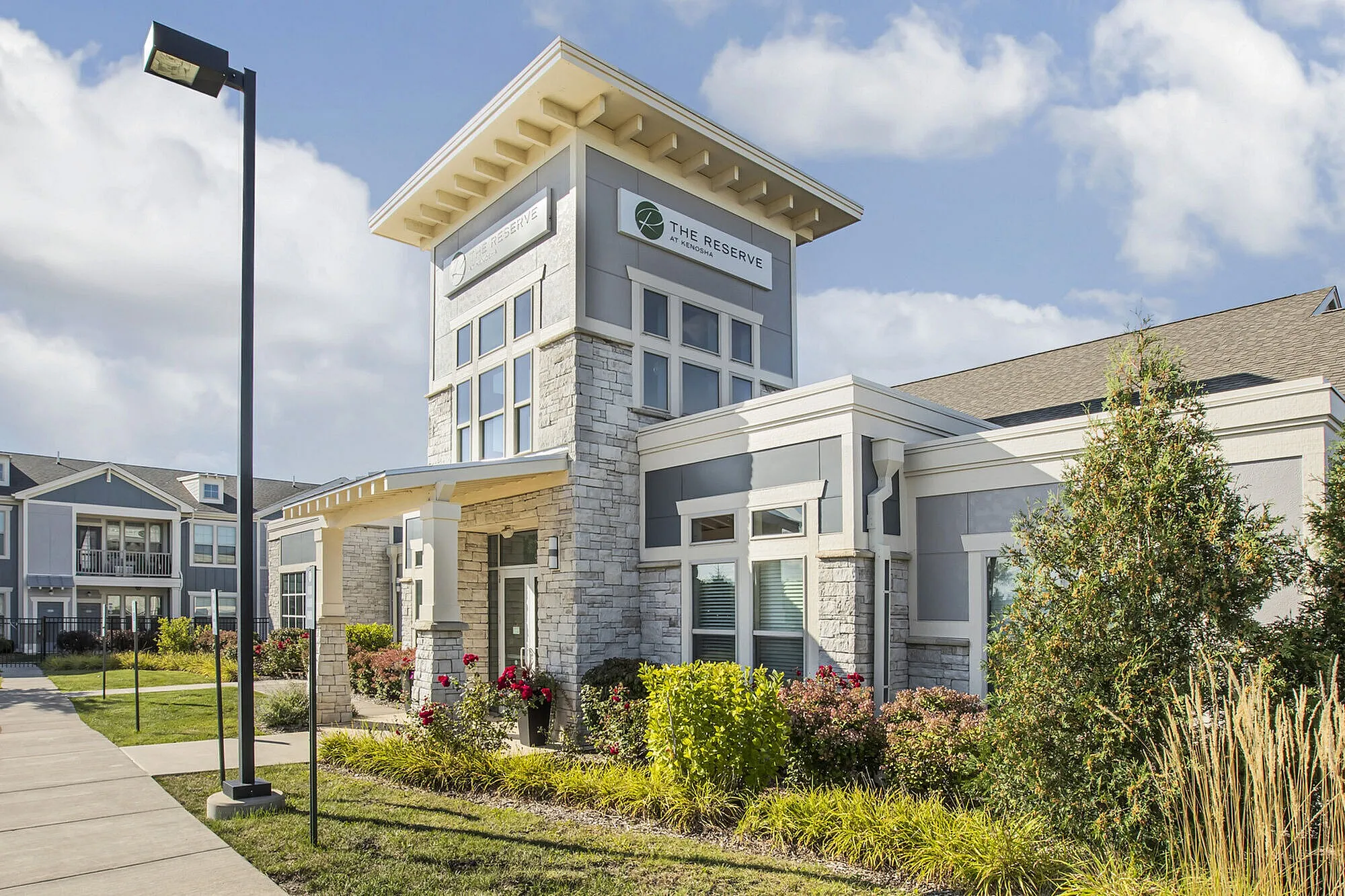Elegant apartment complex featuring modern architecture with stone accents, lush landscaping, and a welcoming entrance.